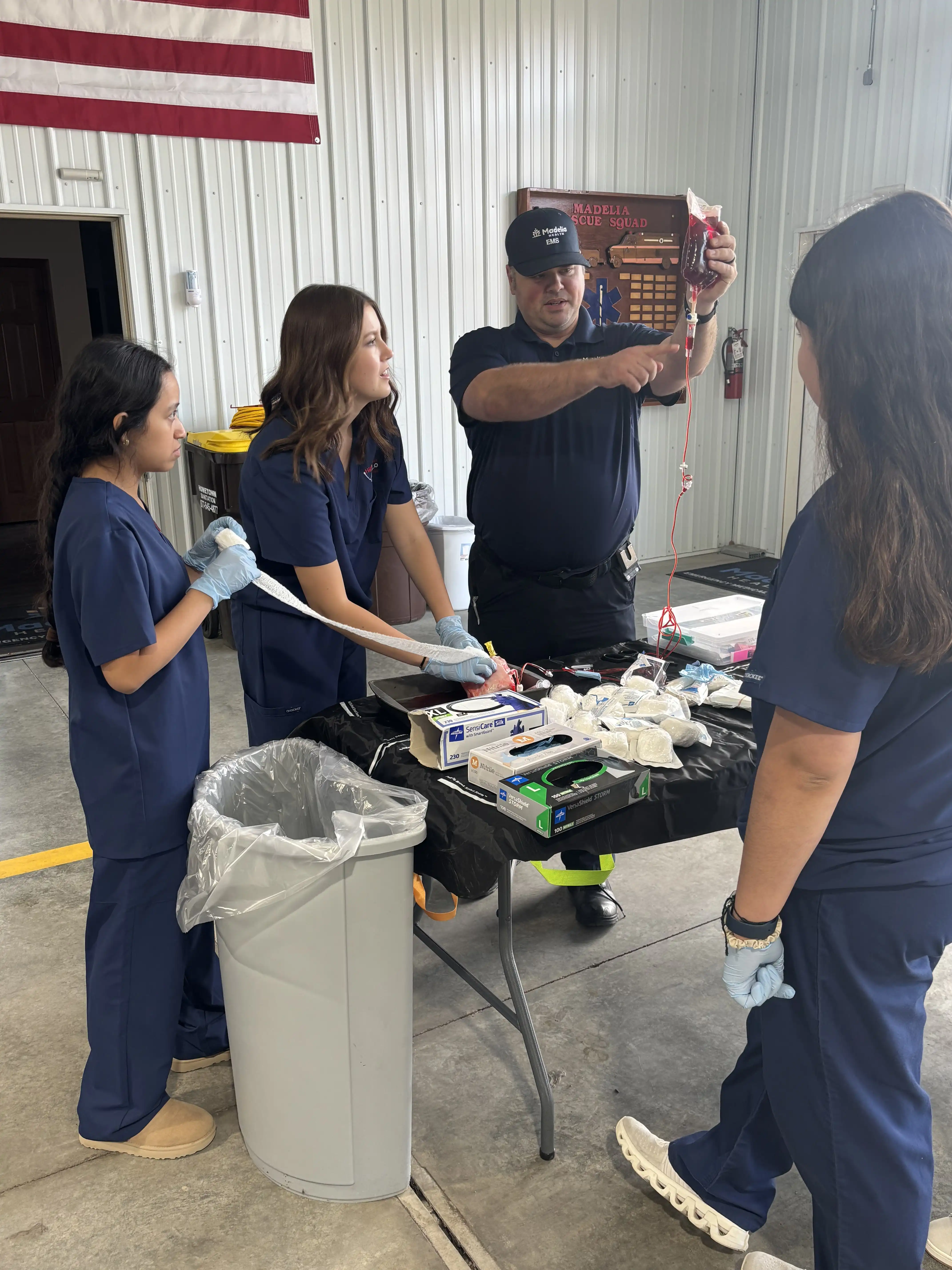 Group of 3 students standing around a table with an adult showing them a blood bag and the IV for body