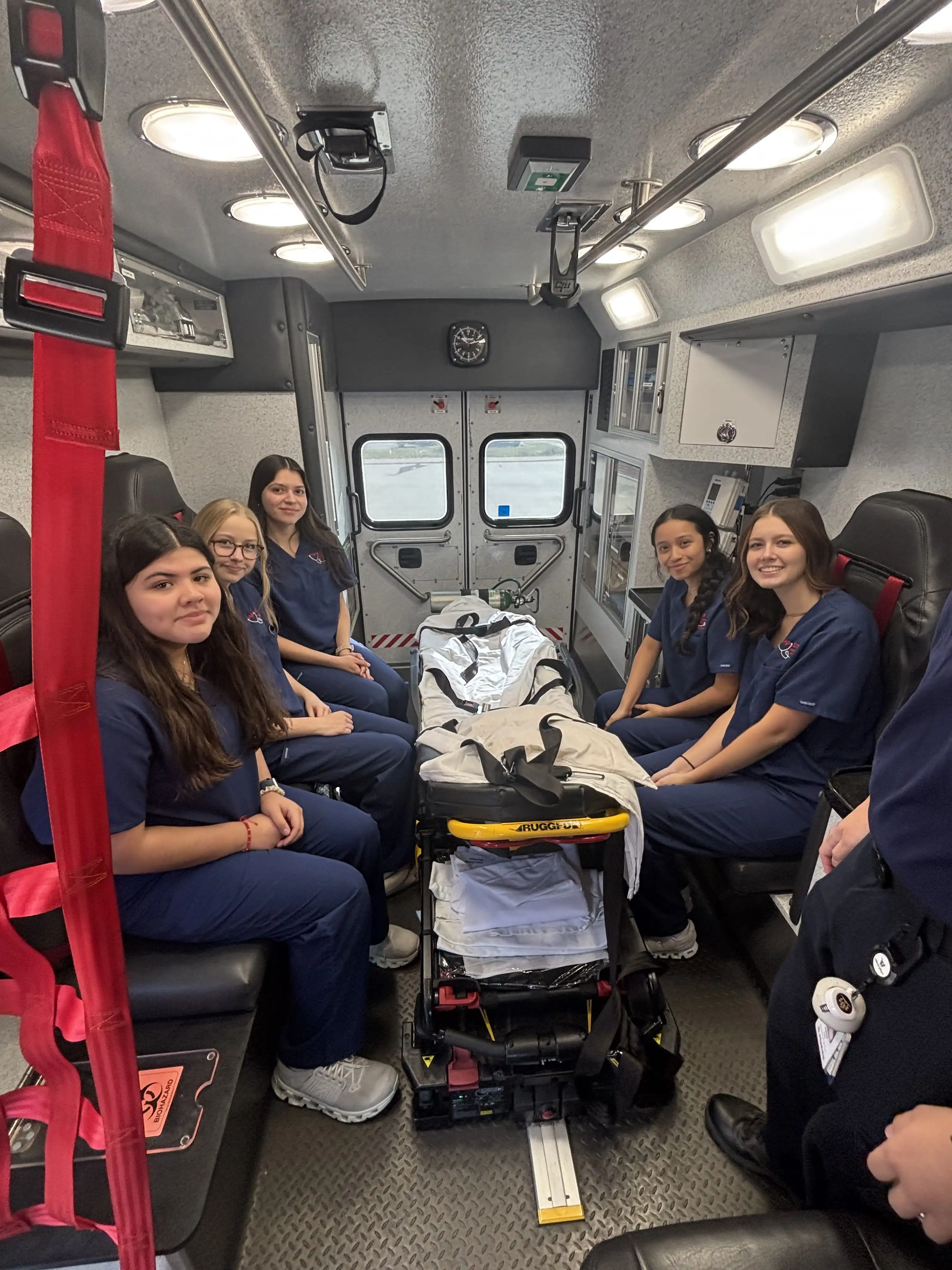 A group of 5 students sitting on either side of a stretcher in the back of the ambulance