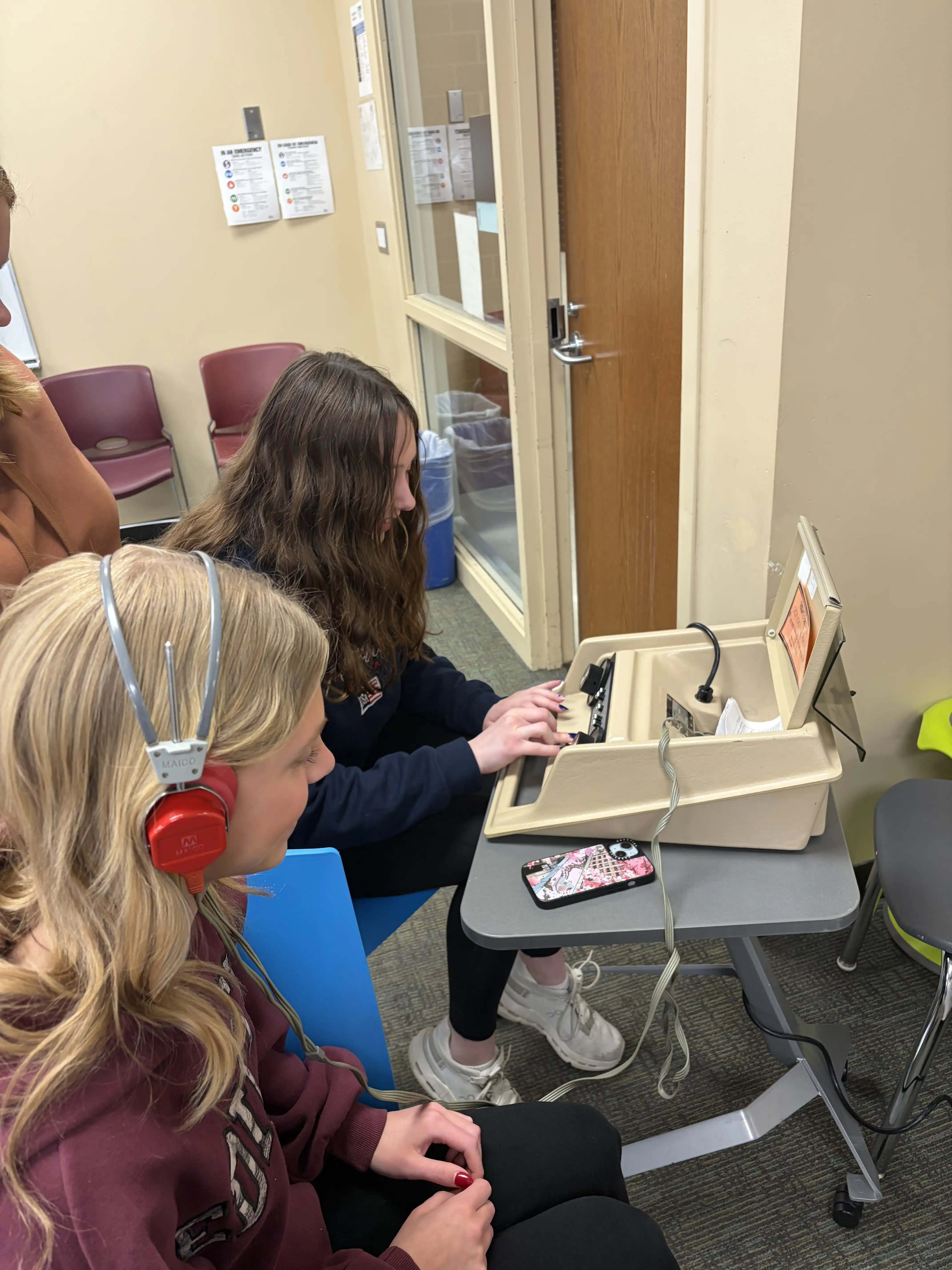 two students sitting at a desk. One student with headphones on to listen for sound the other control the sound for a hearing test