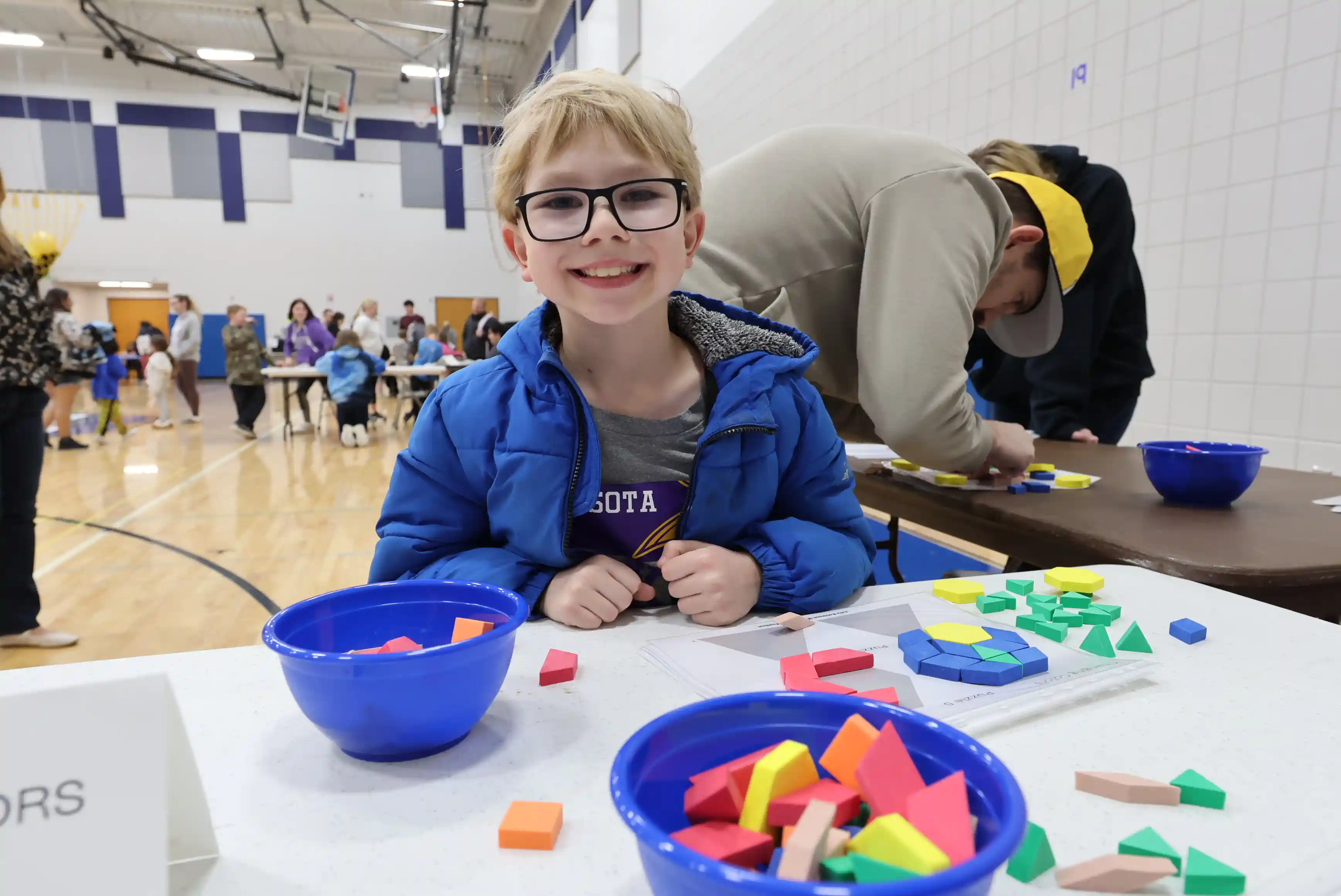 Student smiling while working on a math problem with shapes