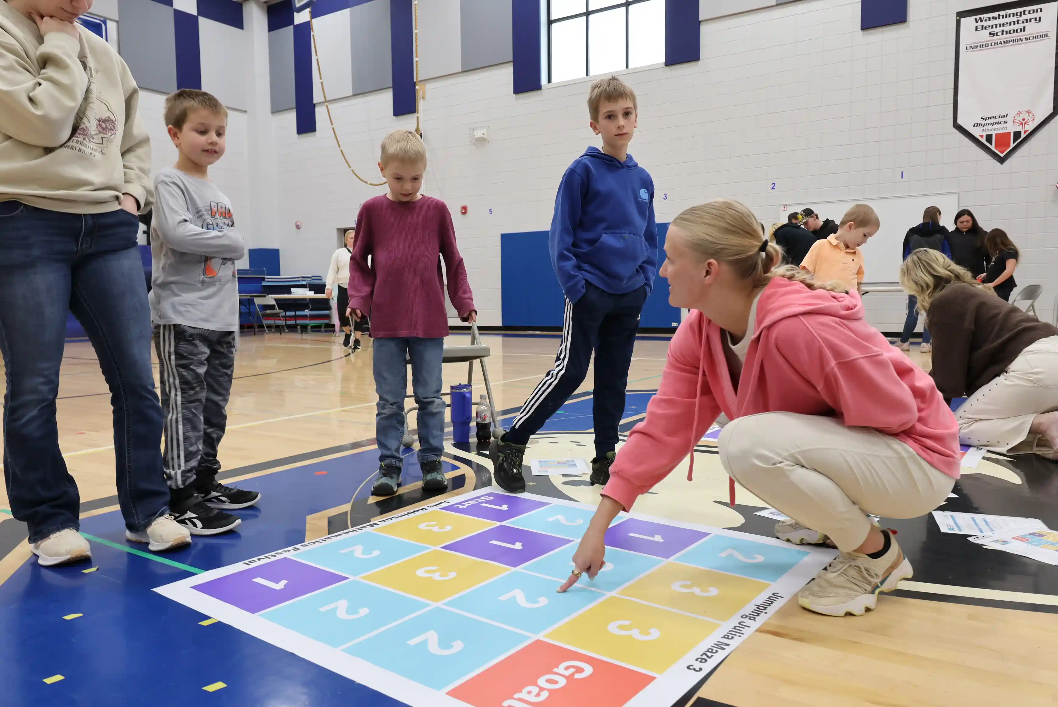 Students walking through a math chart game on the floor and an adult providing instructions