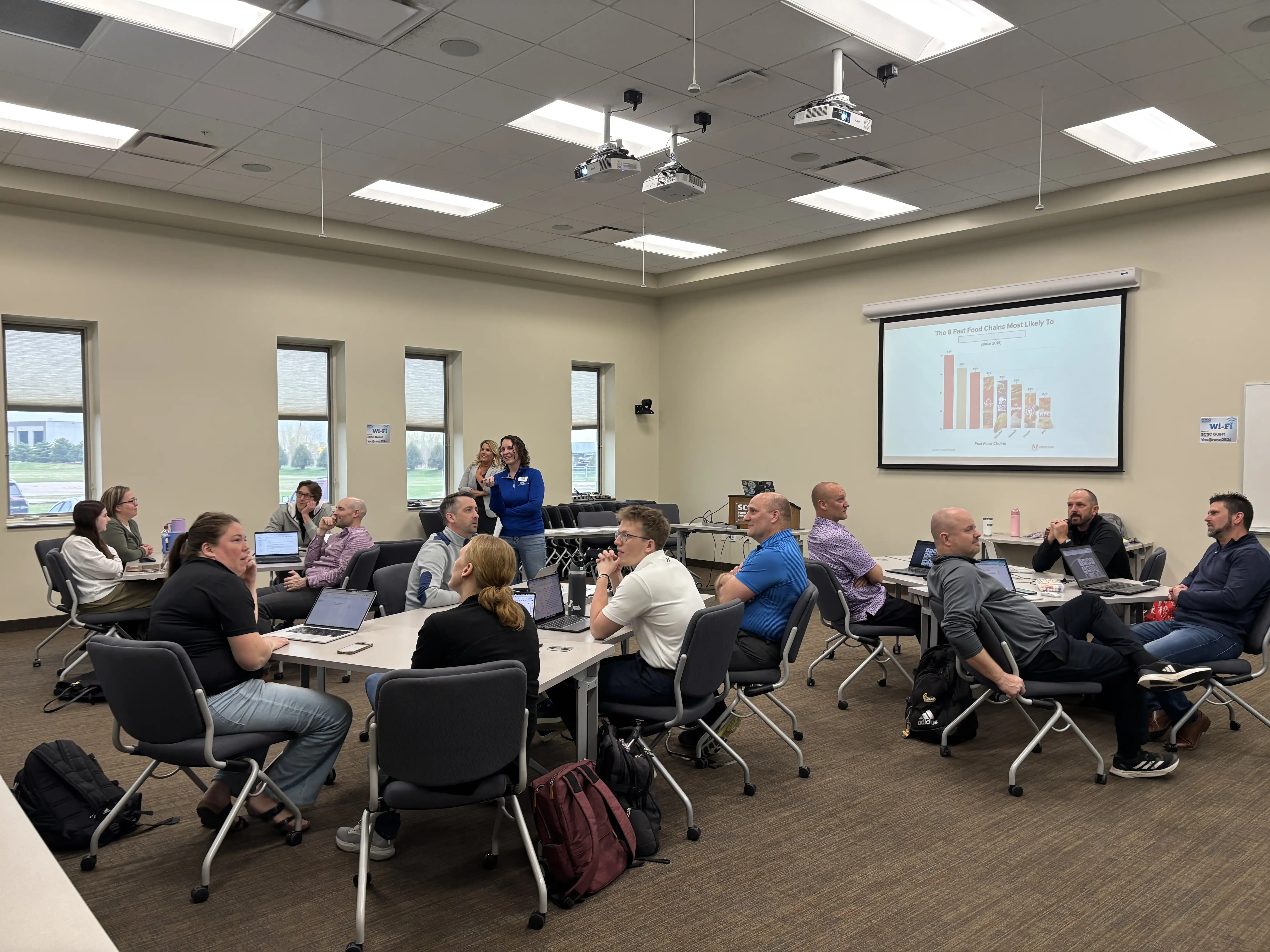 Teachers at tables pods listening to 2 presenters