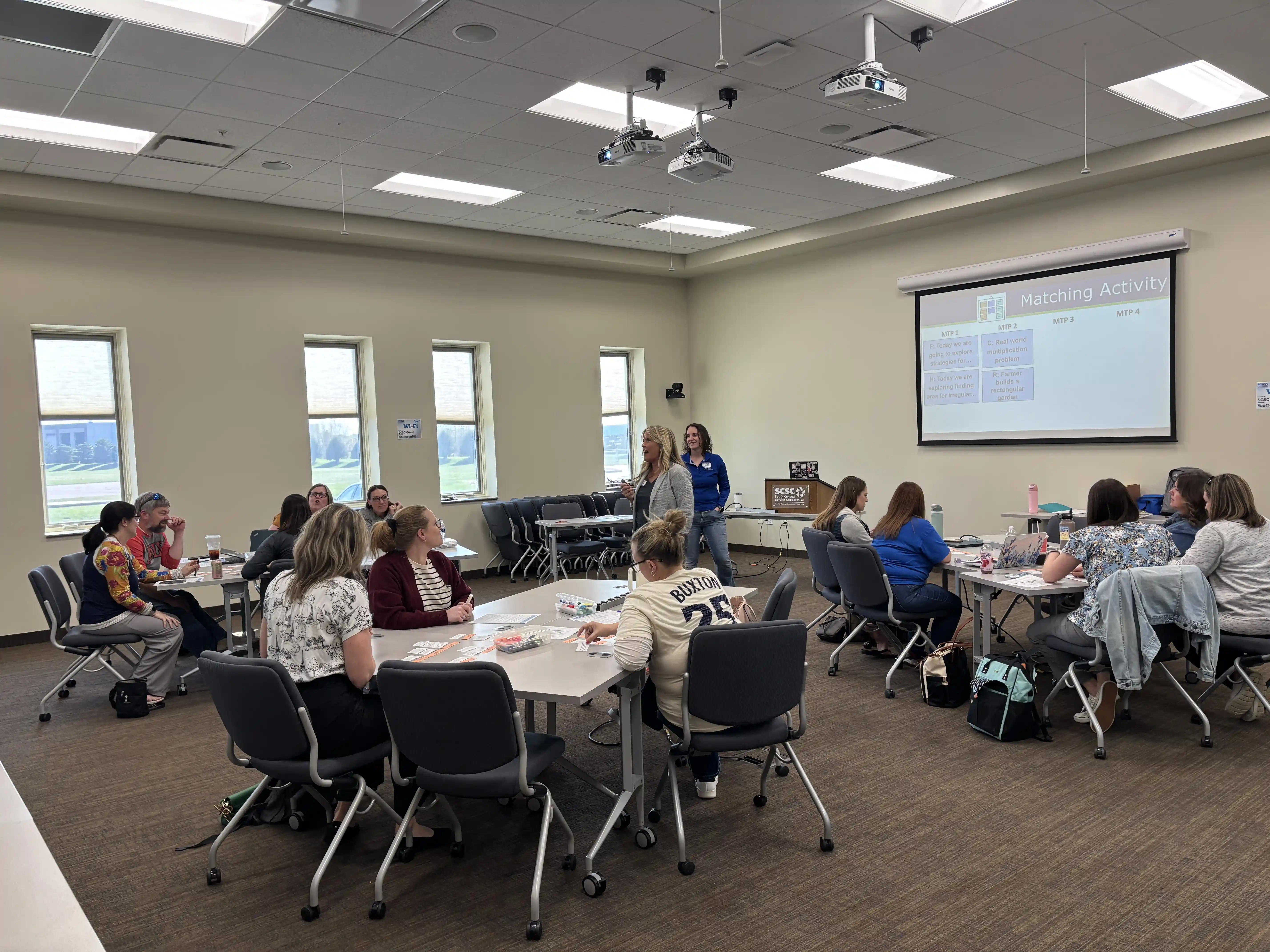 Teachers at tables pods listening to 2 presenters
