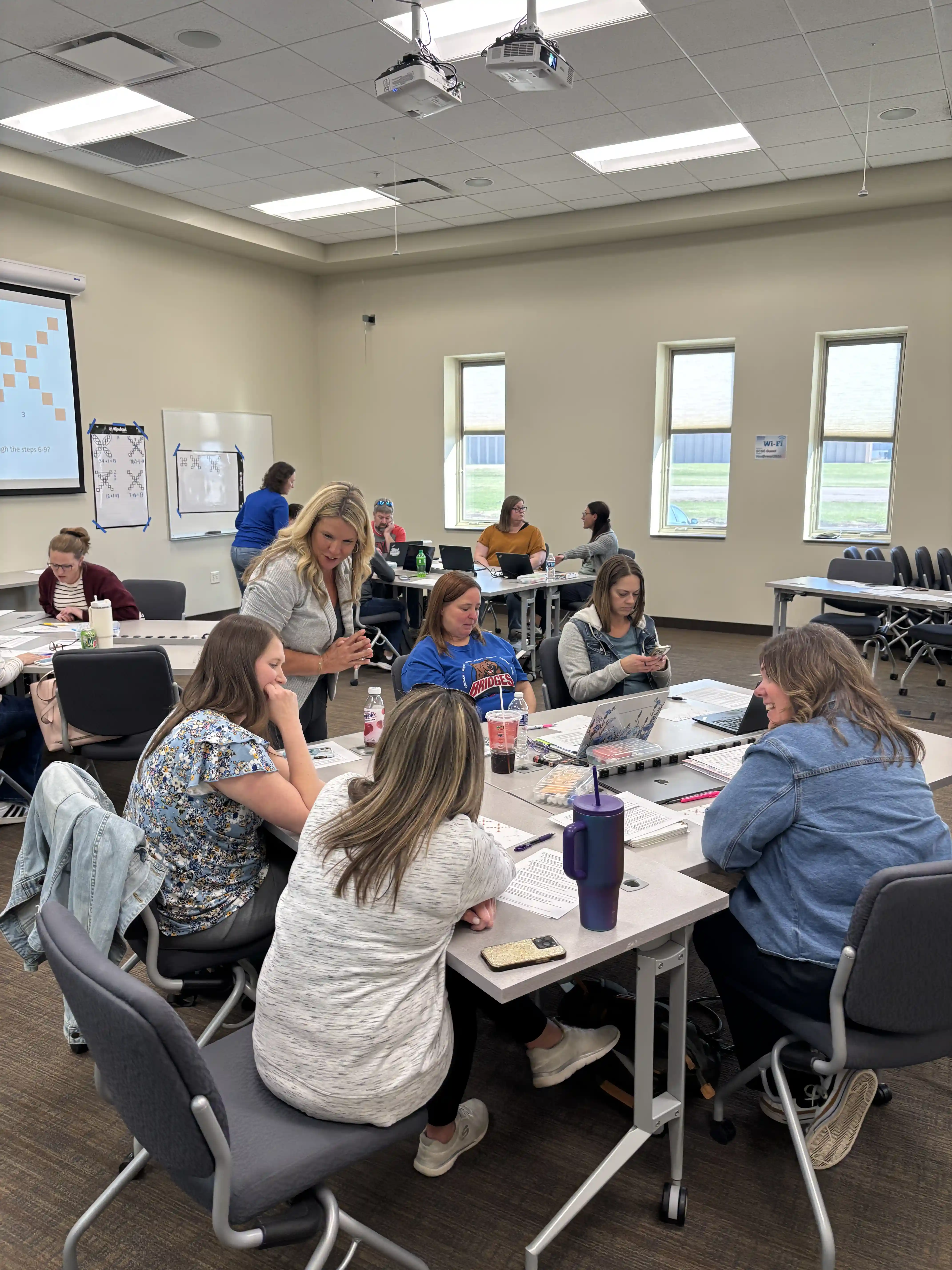 Teachers at tables pods listening to 2 presenters