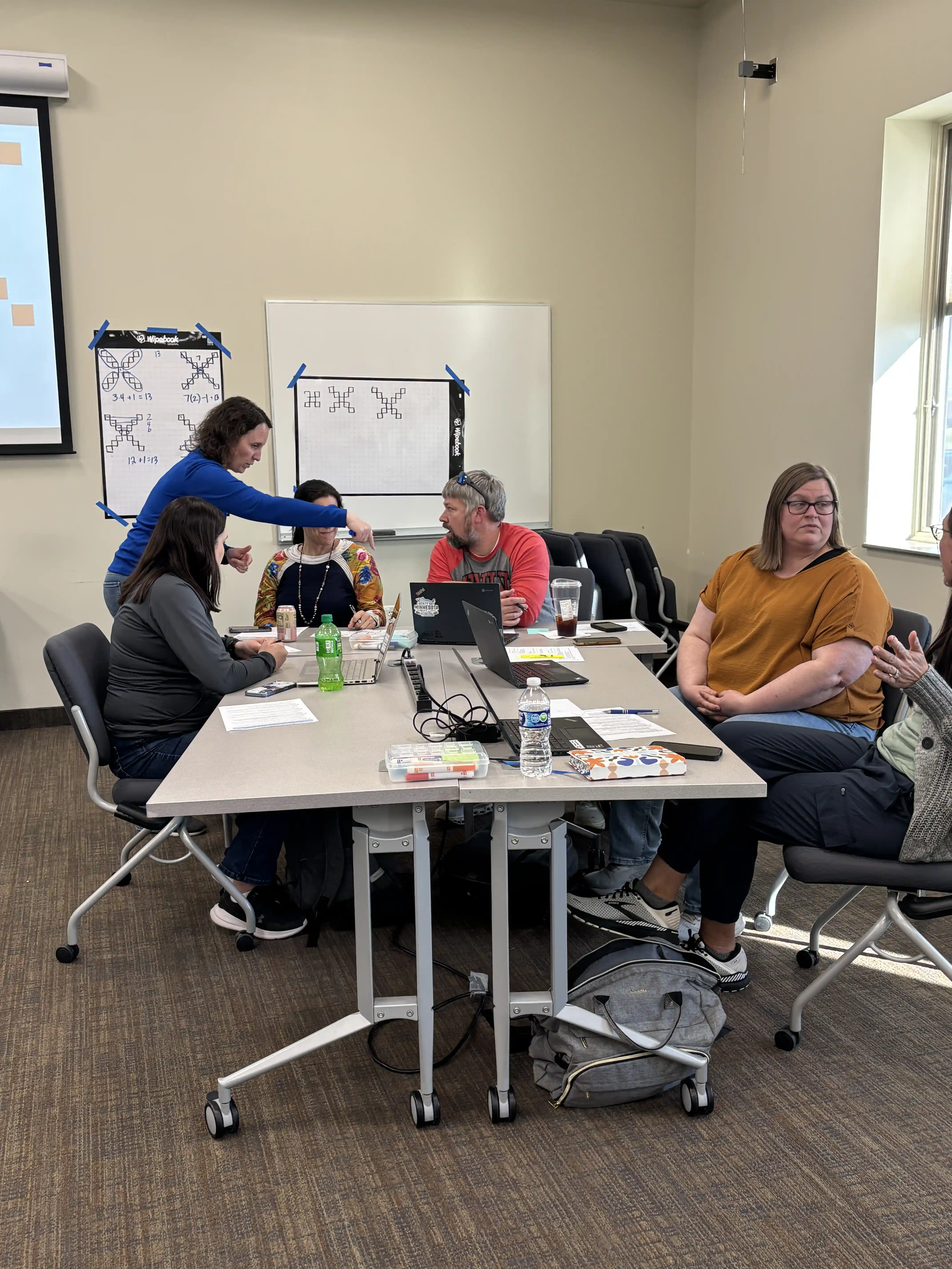 Teachers at tables pods listening to 2 presenters