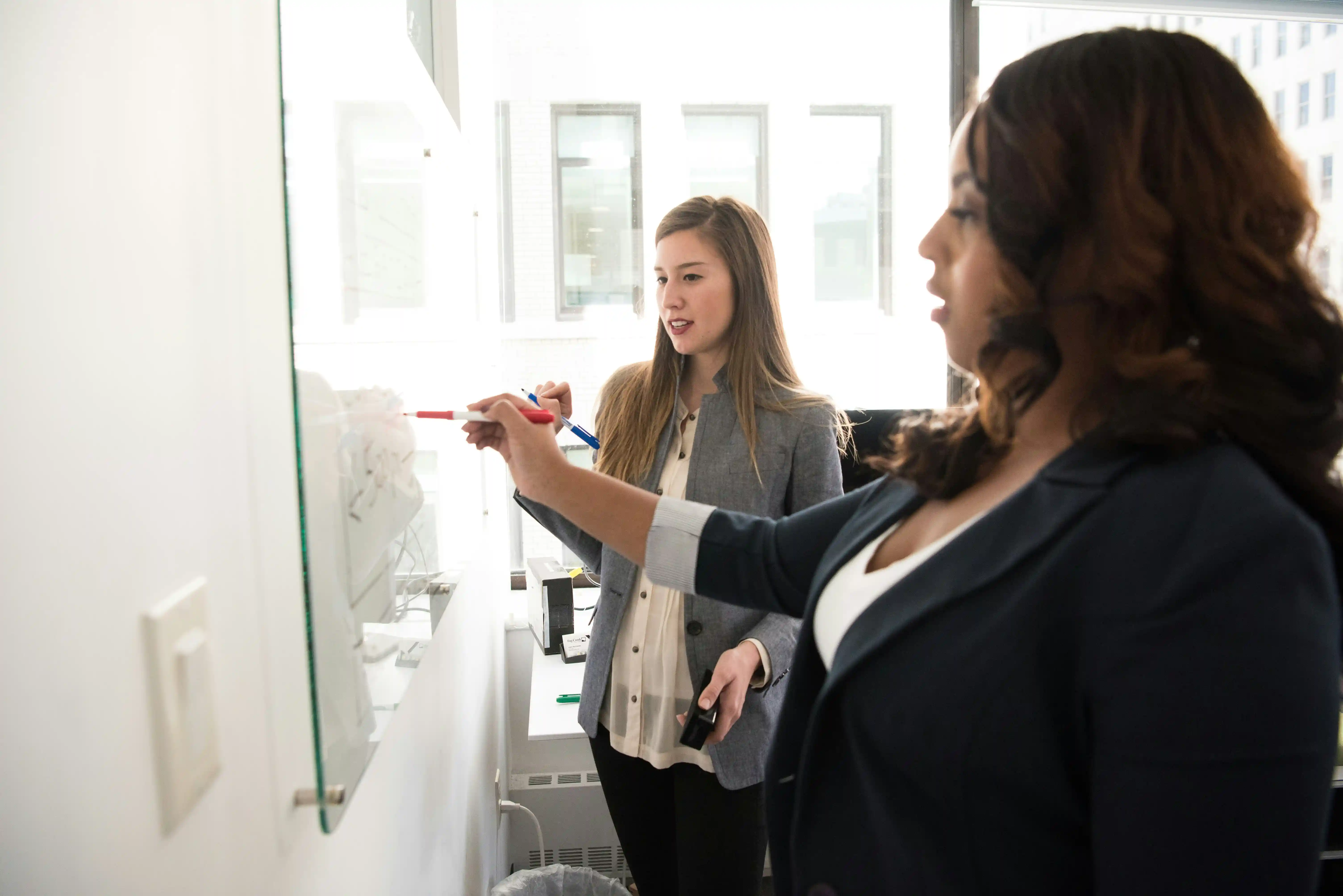 2 women working on a project on a whiteboard together