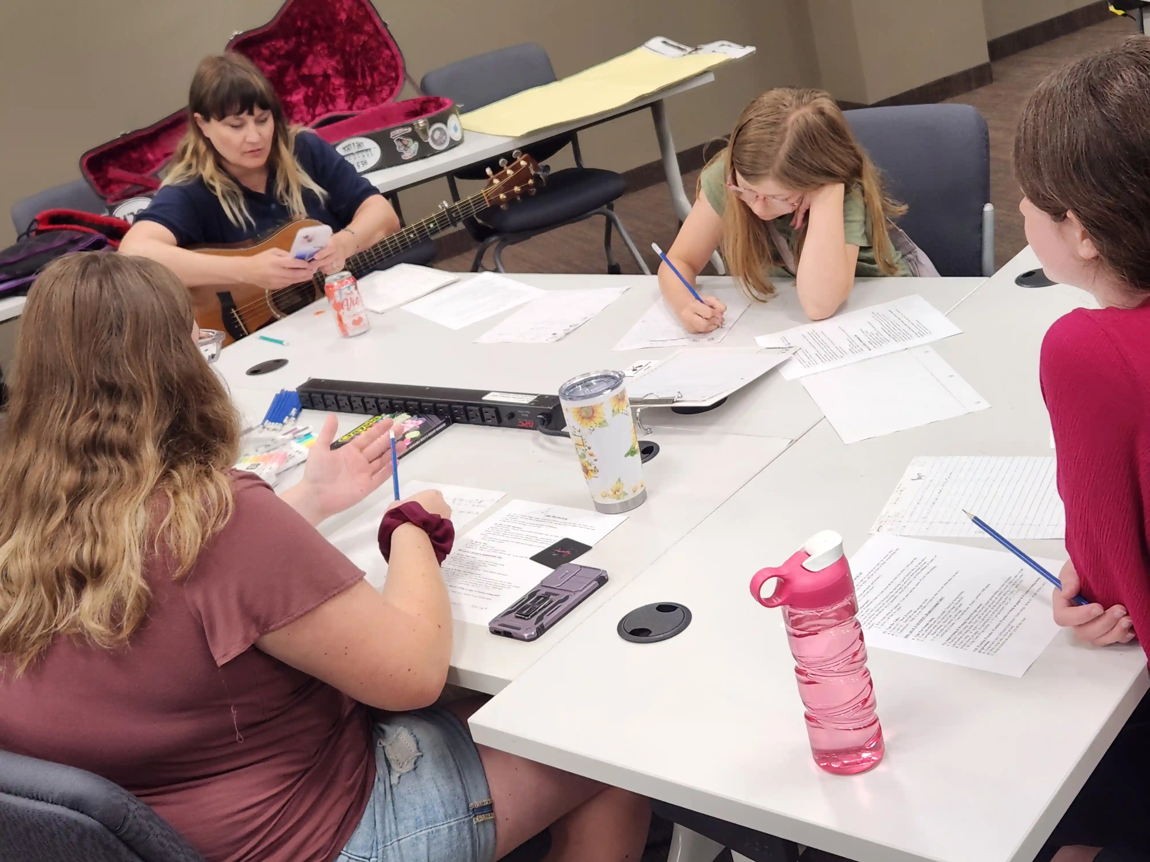 students and adults sitting around a table writing music lyrics