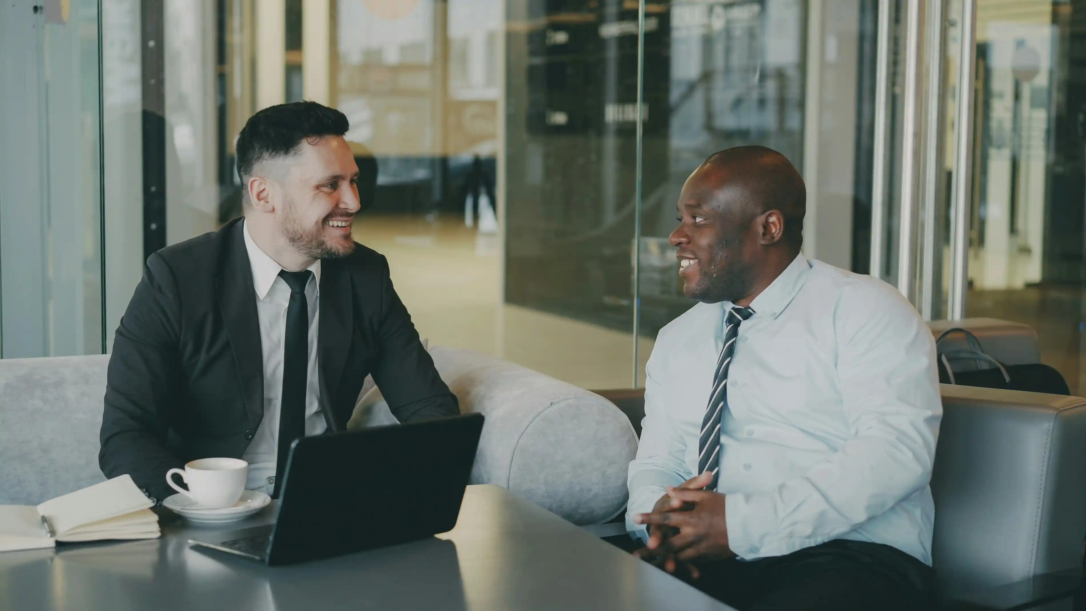 2 people sitting at a table talking with a computer