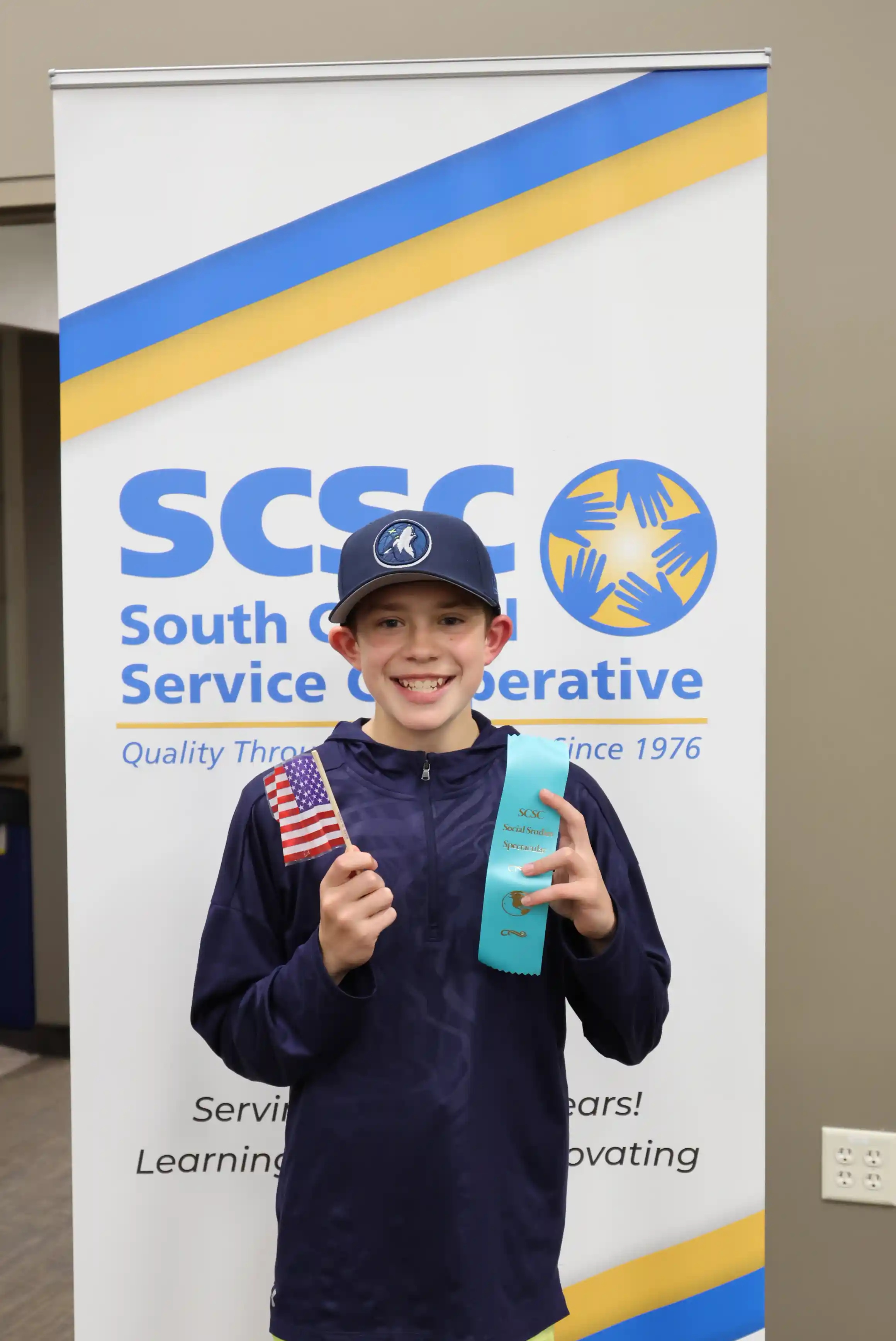 student posing for picture holding a ribbon and an American flag