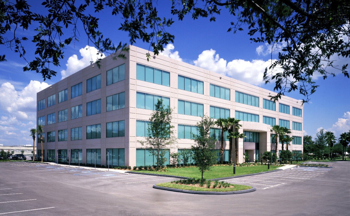 Modern three-story office building with large blue-tinted windows and surrounding parking lot.