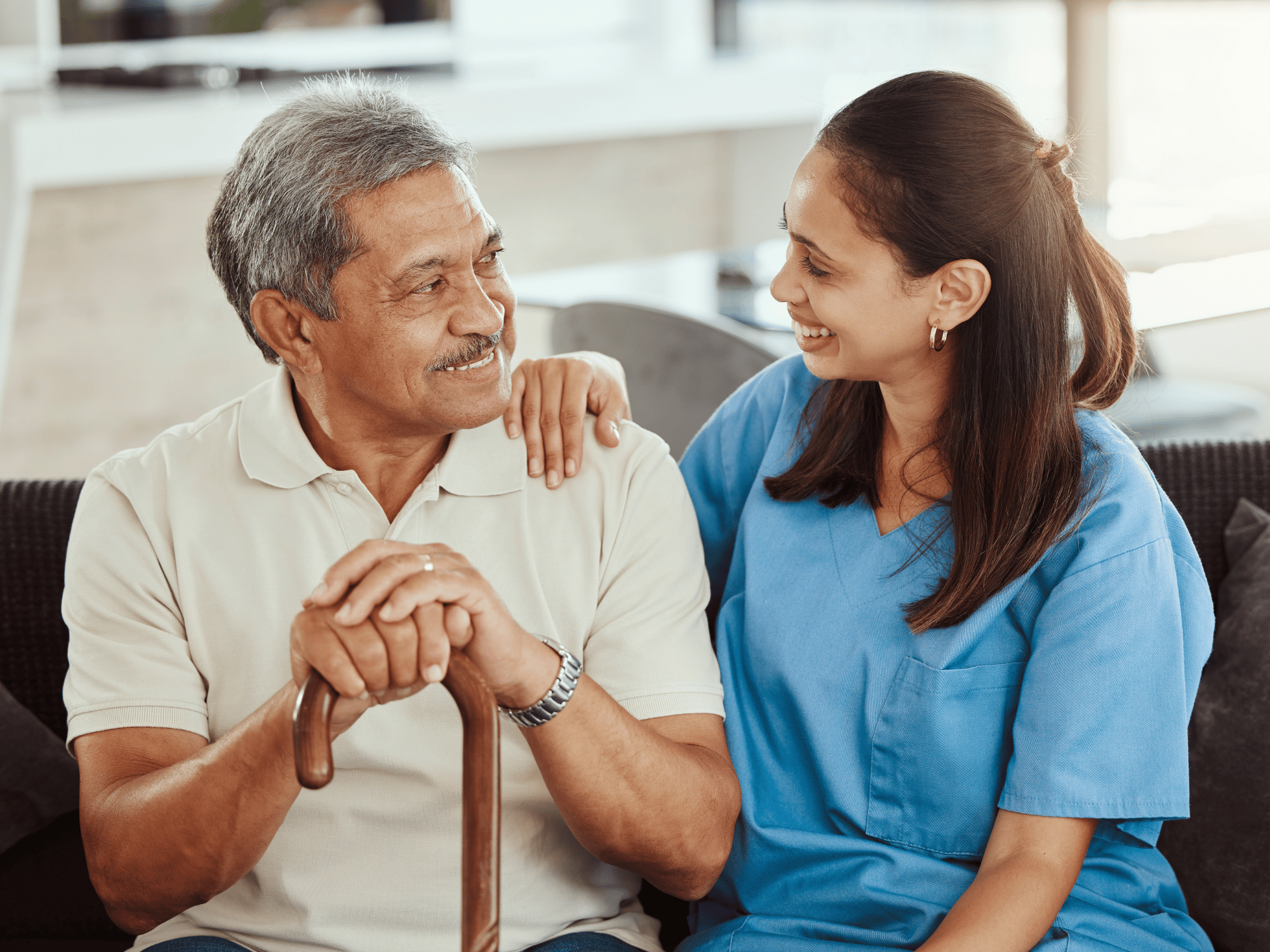 elderly man and caregiver in blue scrubs smiling at eachother