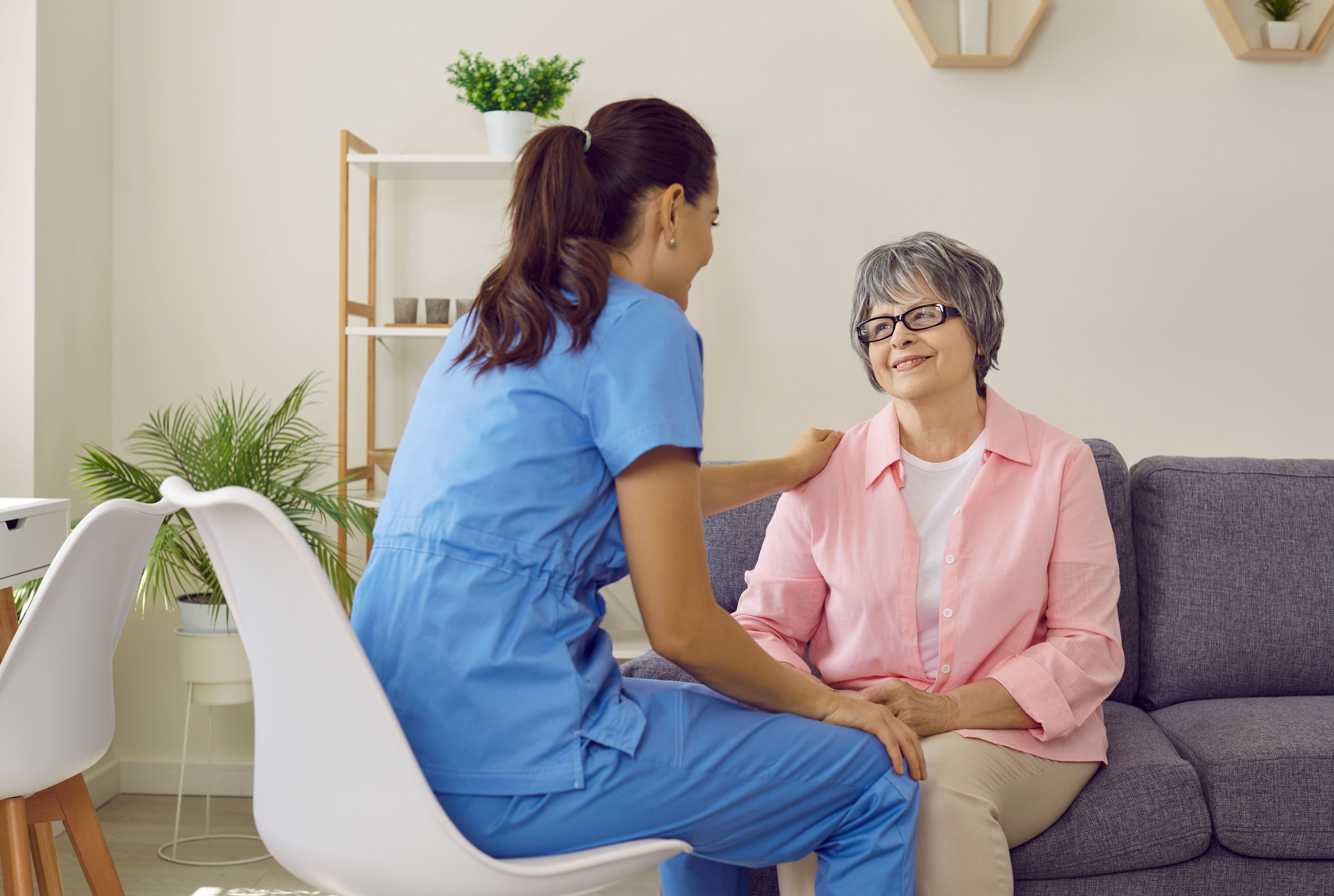 Young healthcare professional at home respectfully communicates with an elderly woman with glasses, conveying a good mood and a positive attitude. The concept of psychological health