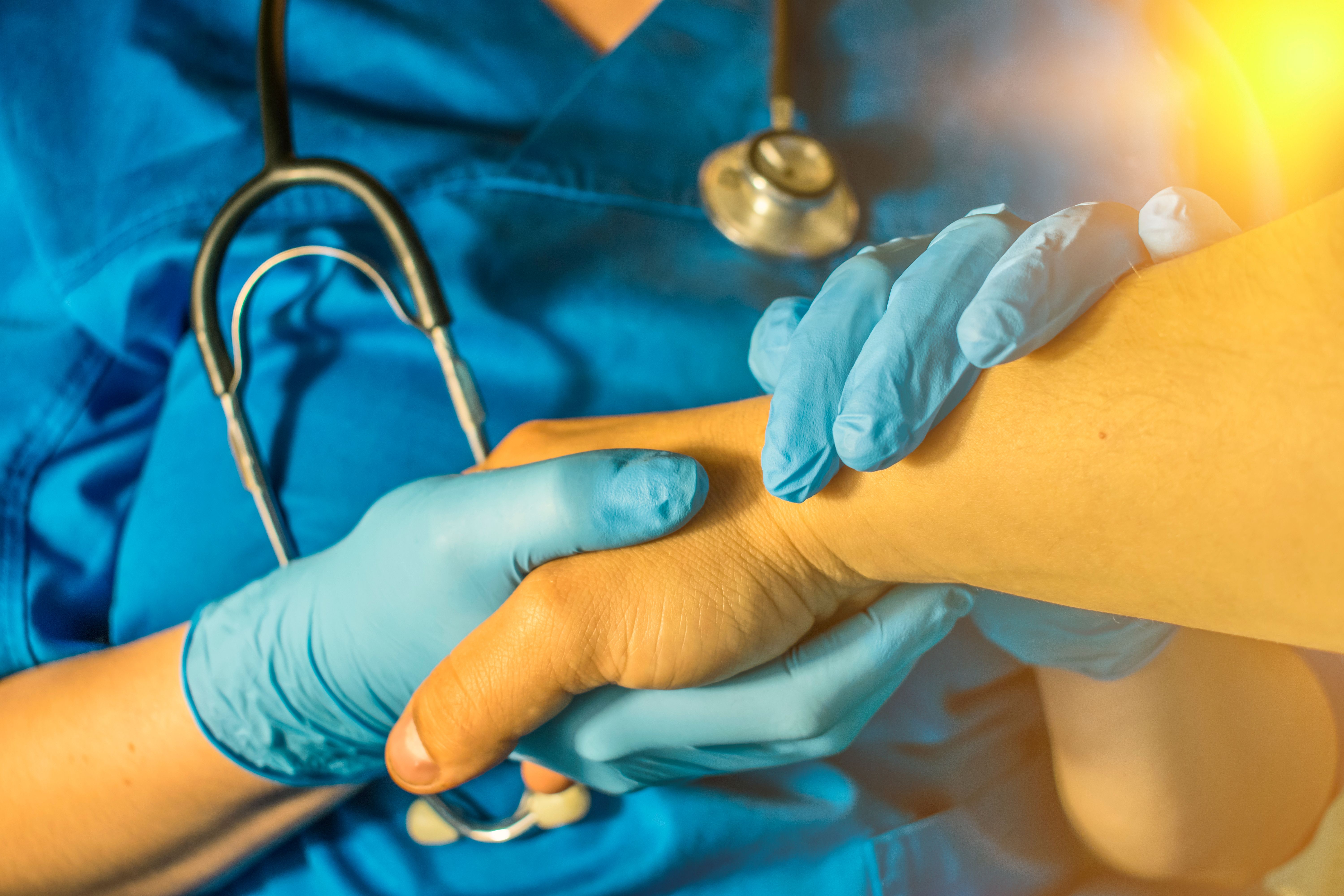 Healthcare professional's gloved hand holding a patient's hand