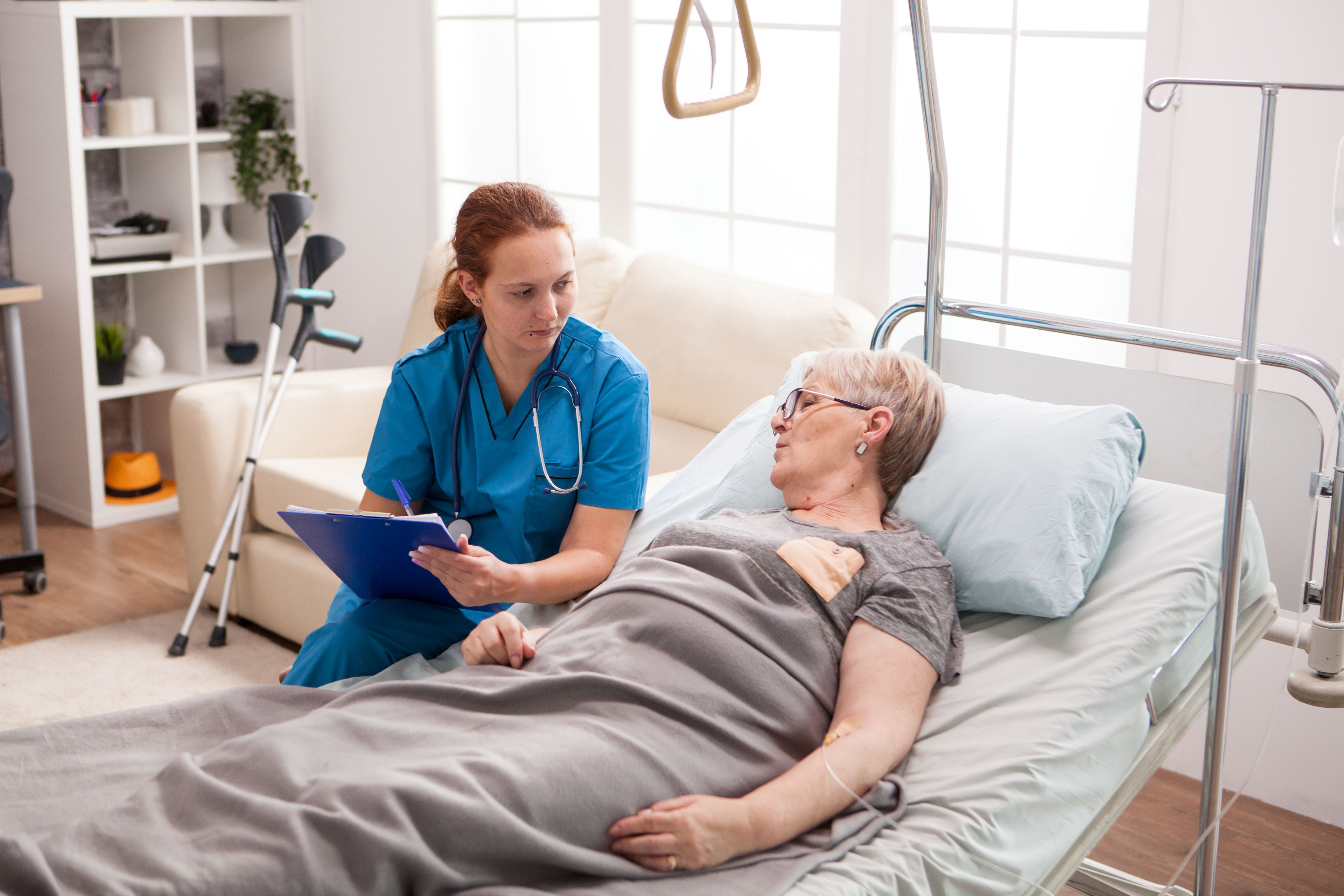 Female caregiver with clipboard talking with sick woman in home