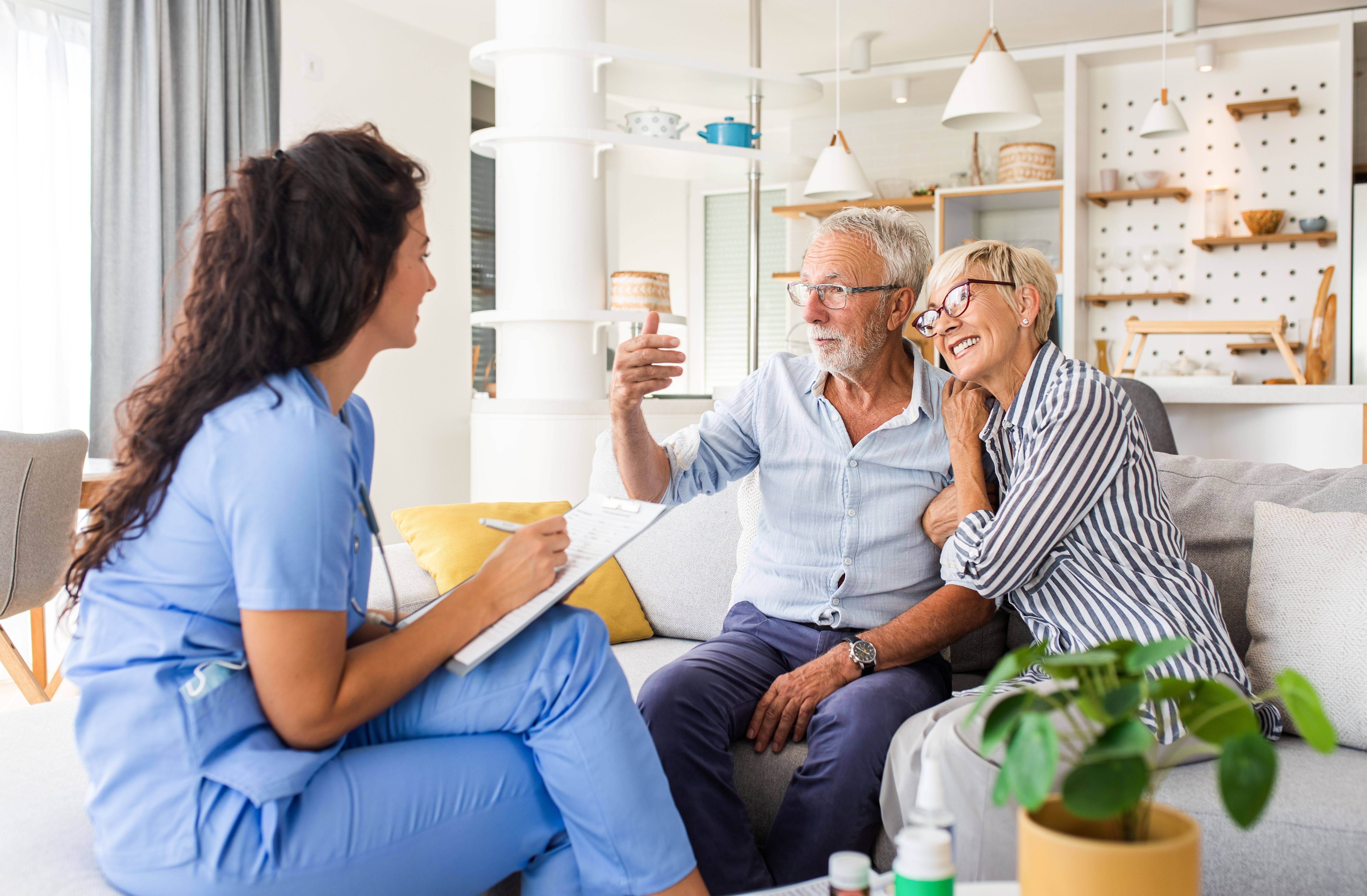 Female nurse talking to seniors patients while being in a home visit, senior couple shows signs of happiness