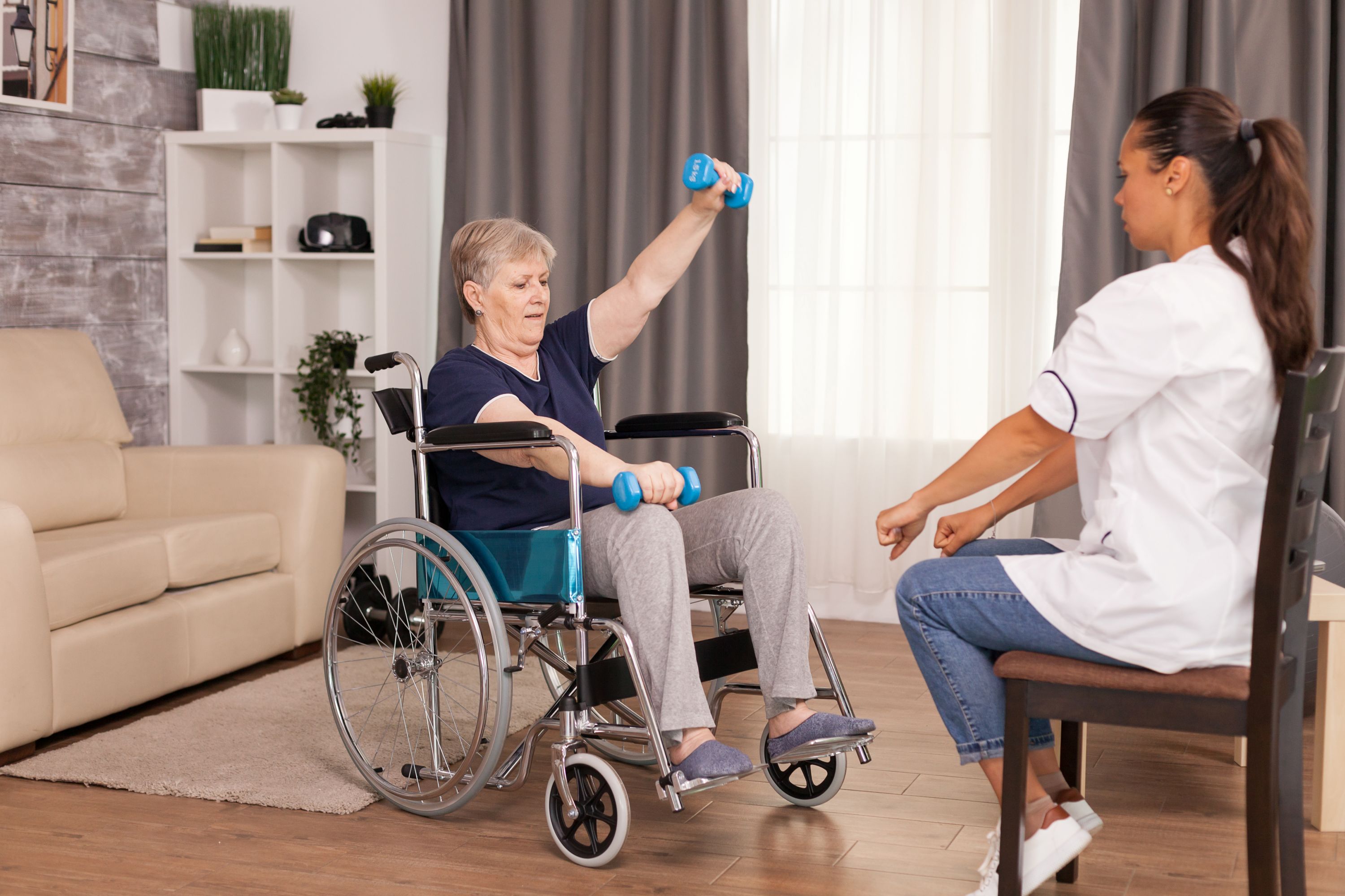 senior woman using weights with the help of nurse. Disabled handicapped old person recovering professional help nurse, nursing retirement home treatment and rehabilitation