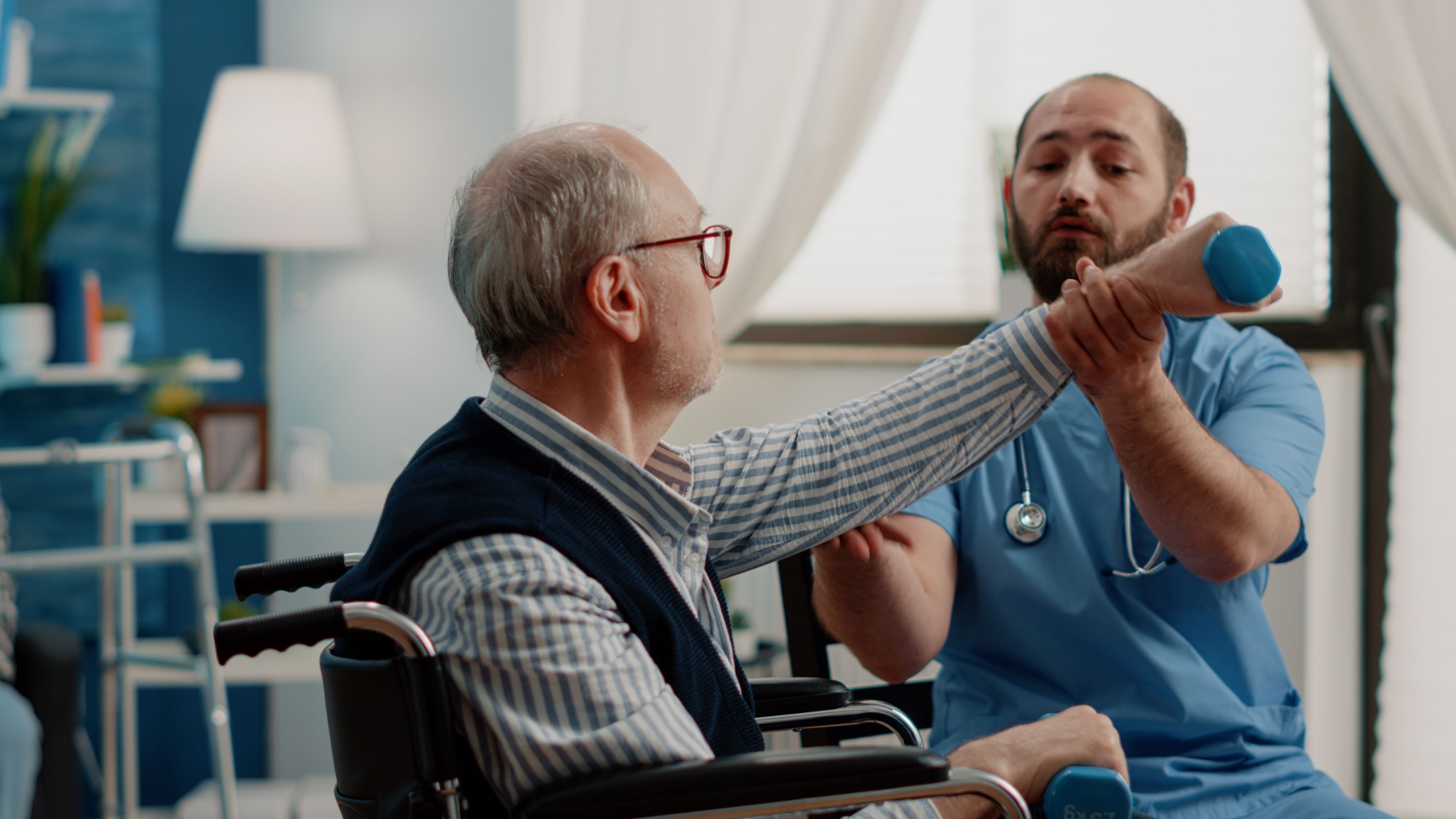 Retired man sitting in wheelchair doing physical exercise for therapy while nurse giving help for activity. 
