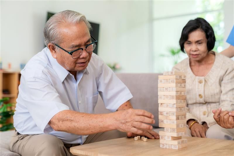 Dementia therapy in playful way. Group of senior elder people stay at nursing home, enjoy activity.relation playing Jenga or tumbling tower wood block game. Training fingers and fine skills