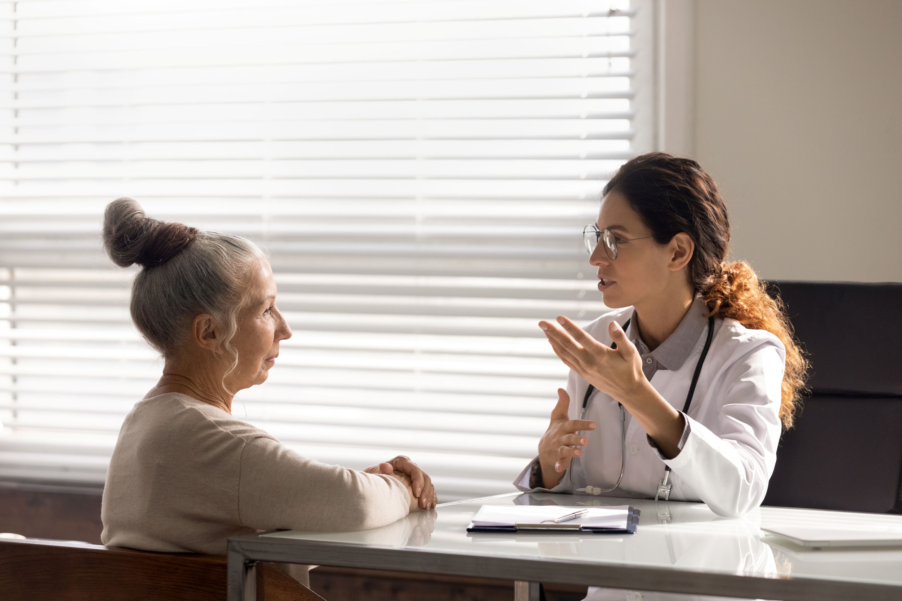 Young therapist talking to senior female patient in home