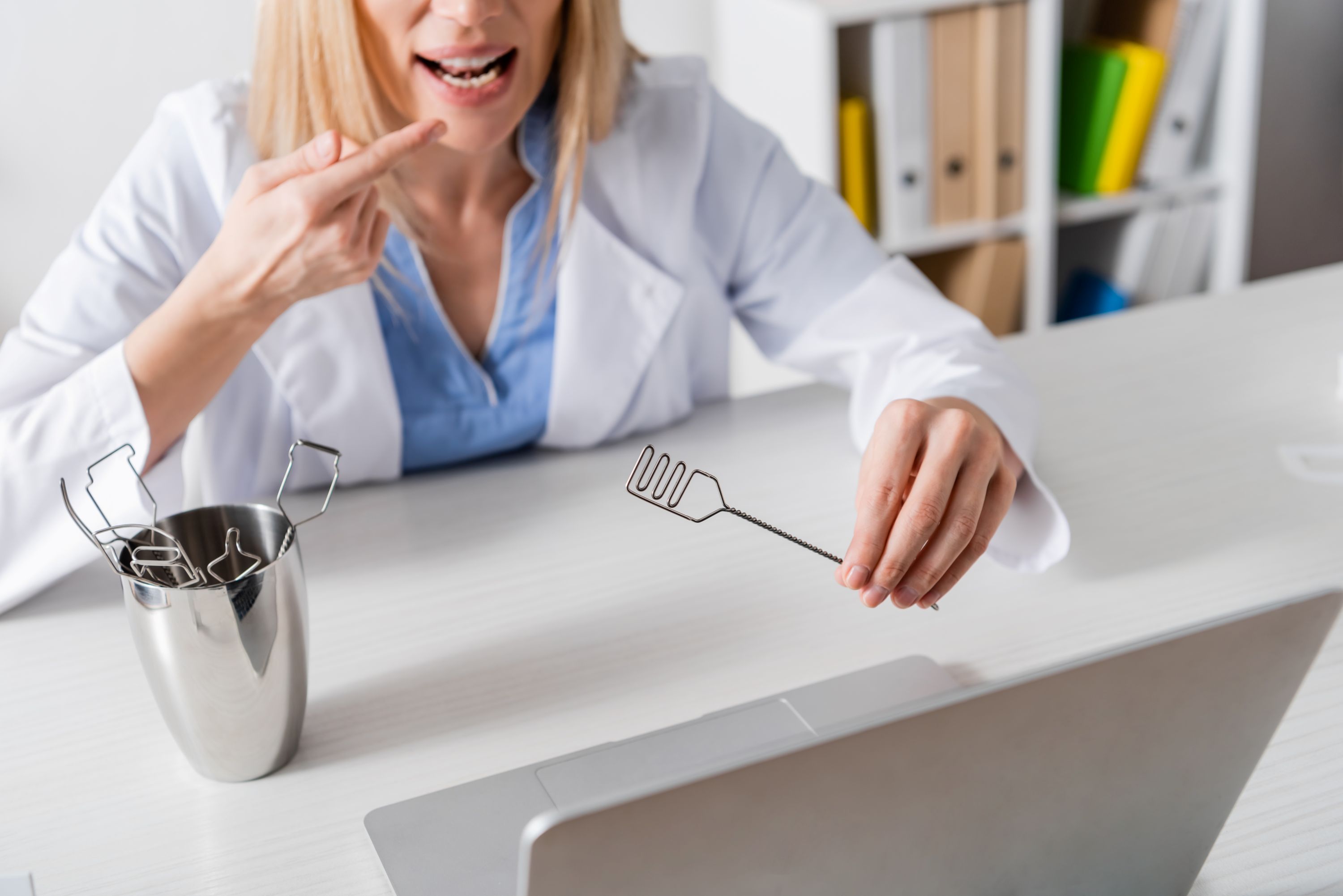 speech therapist pointing at mouth and holding tool during online lesson on laptop