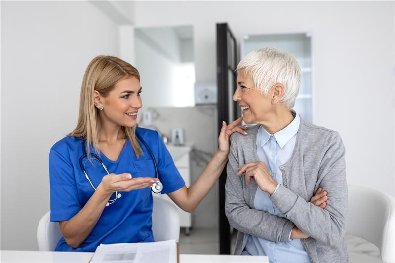Young female medical professional conducting speech therapy session with senior woman client in home