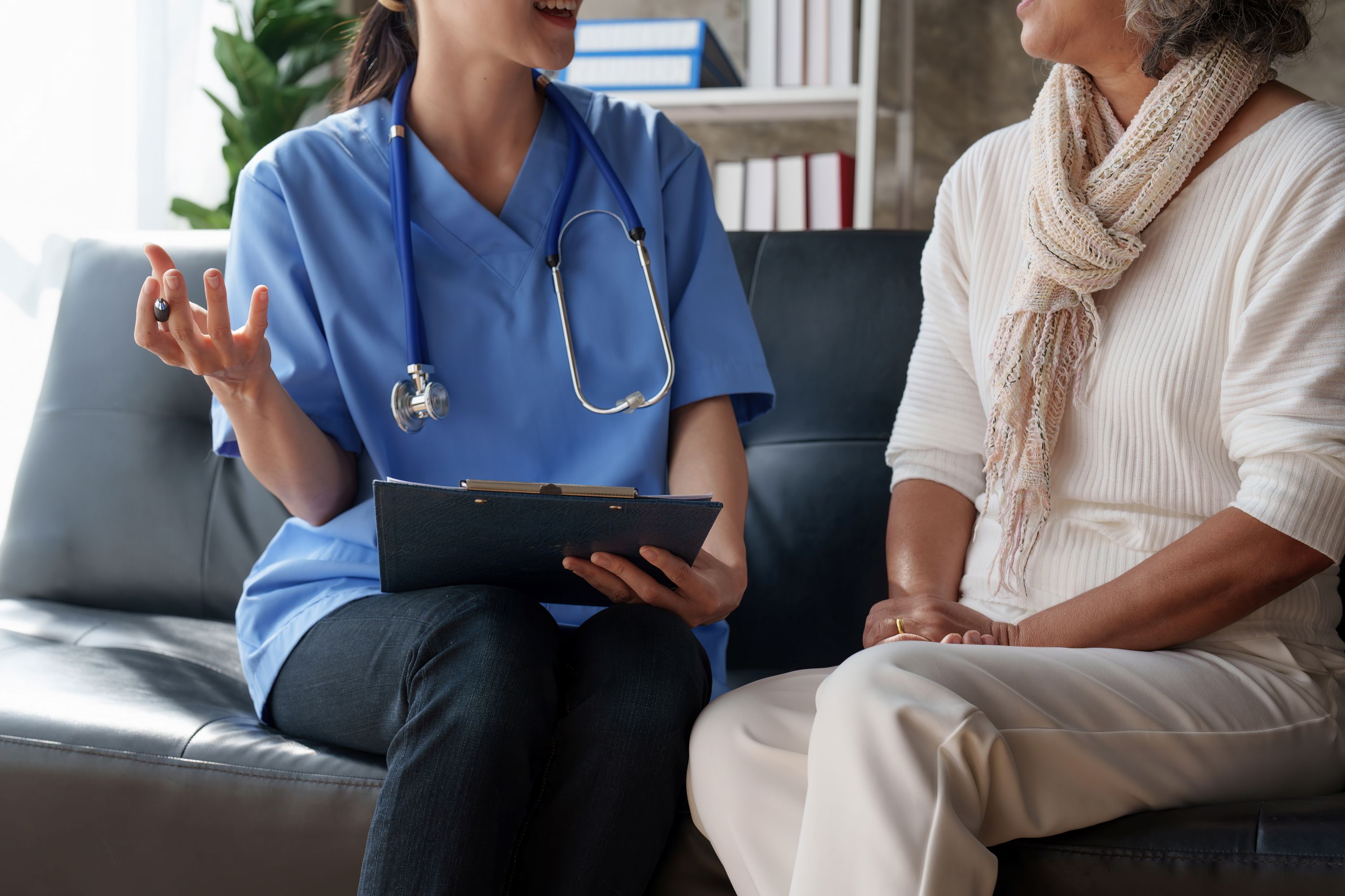 Home healthcare nurse taking notes and speaking with senior adult woman at home