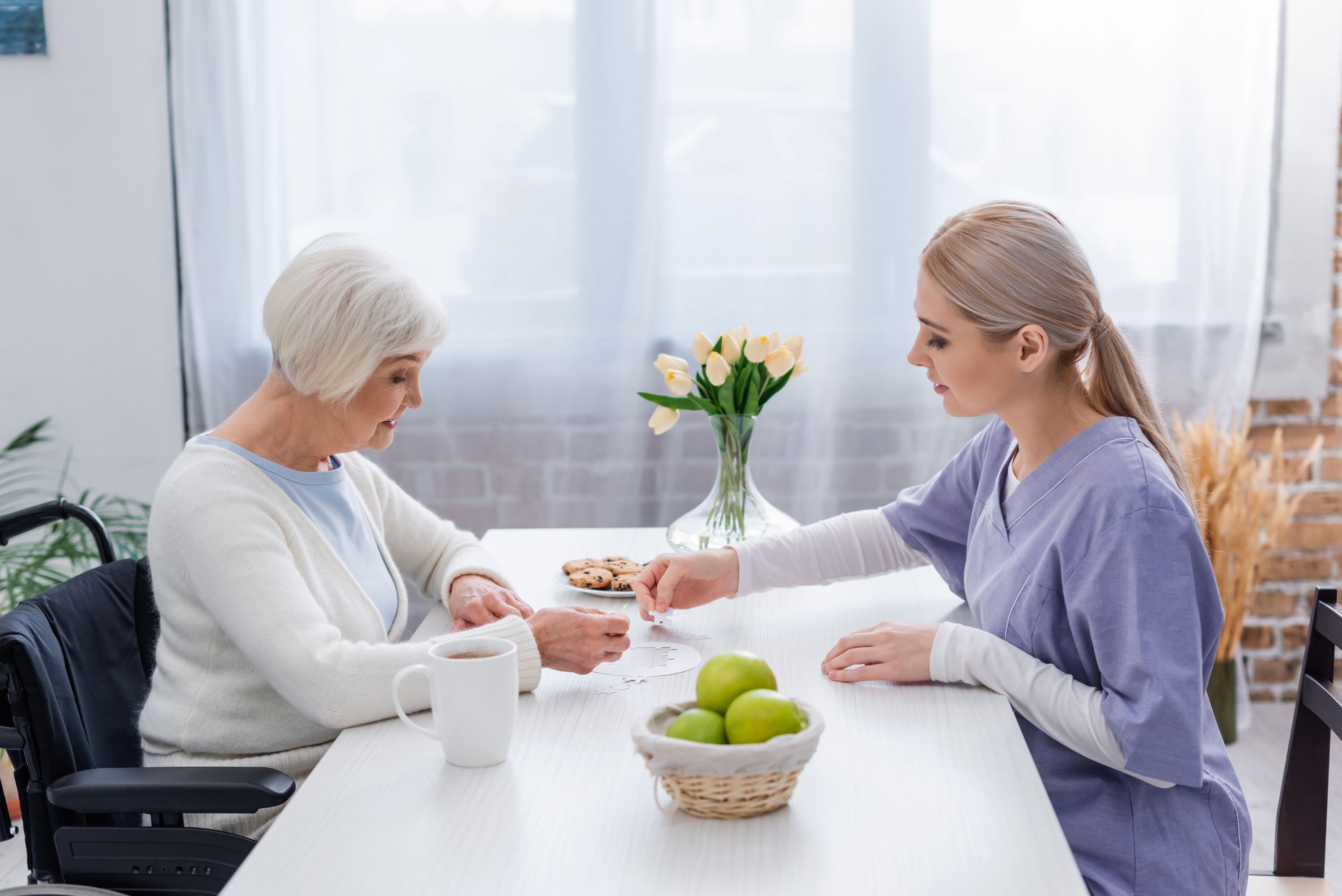 young home healthcare worker playing jigsaw puzzle with handicapper senior woman at home
