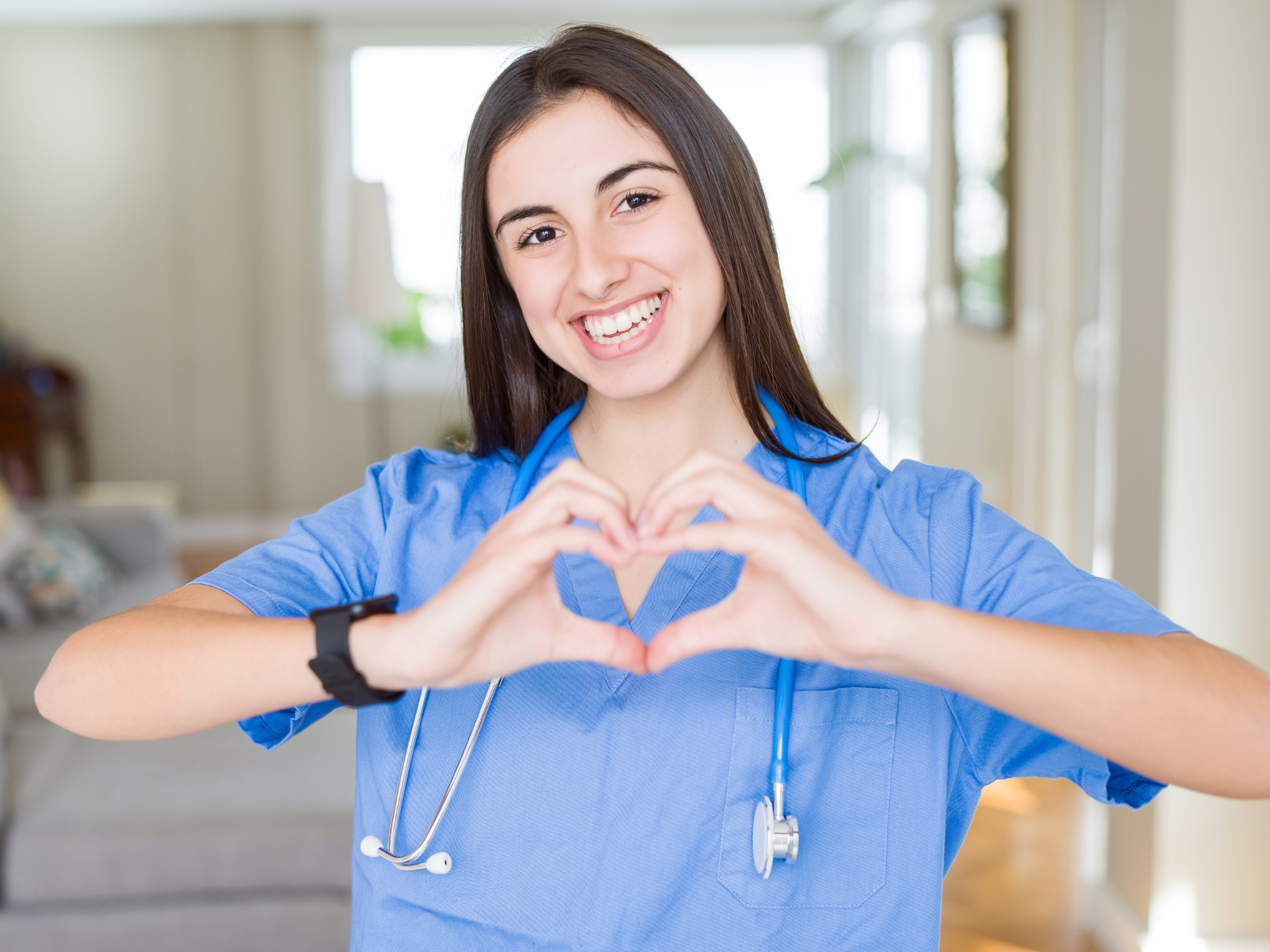 young nurse woman wearing uniform and stethoscope at the clinic smiling in love showing heart symbol and shape with hands.