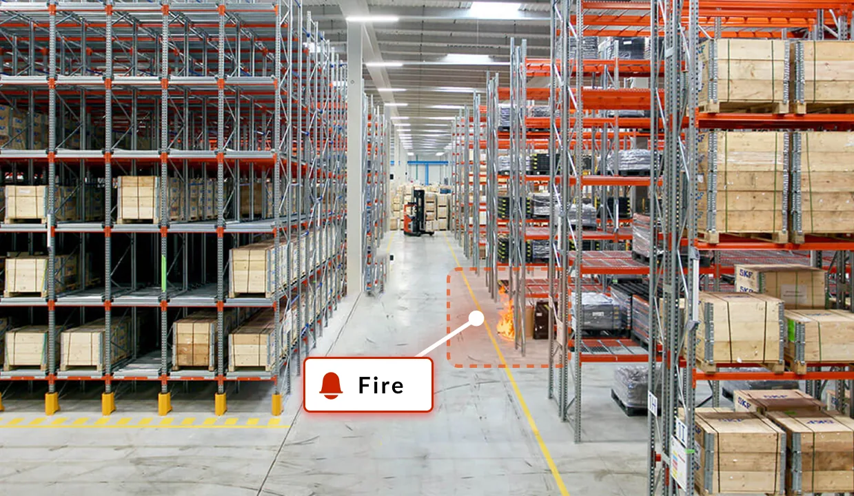 High-bay racking aisle with a small fire flagged by a fire alert card