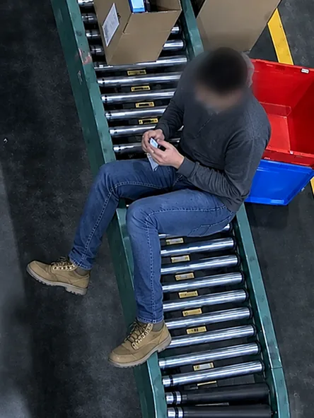 Top-down camera view of a blurred worker sitting on a roller conveyor