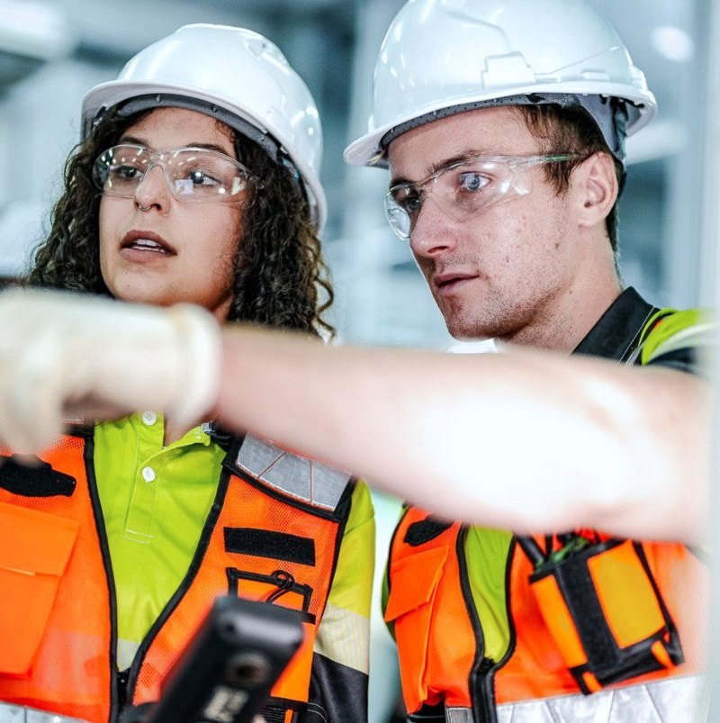 Two safety team members in hard hats reviewing alerts on a handheld device