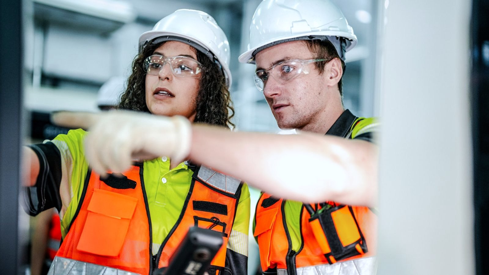 Two safety team members in hard hats reviewing alerts on a handheld device