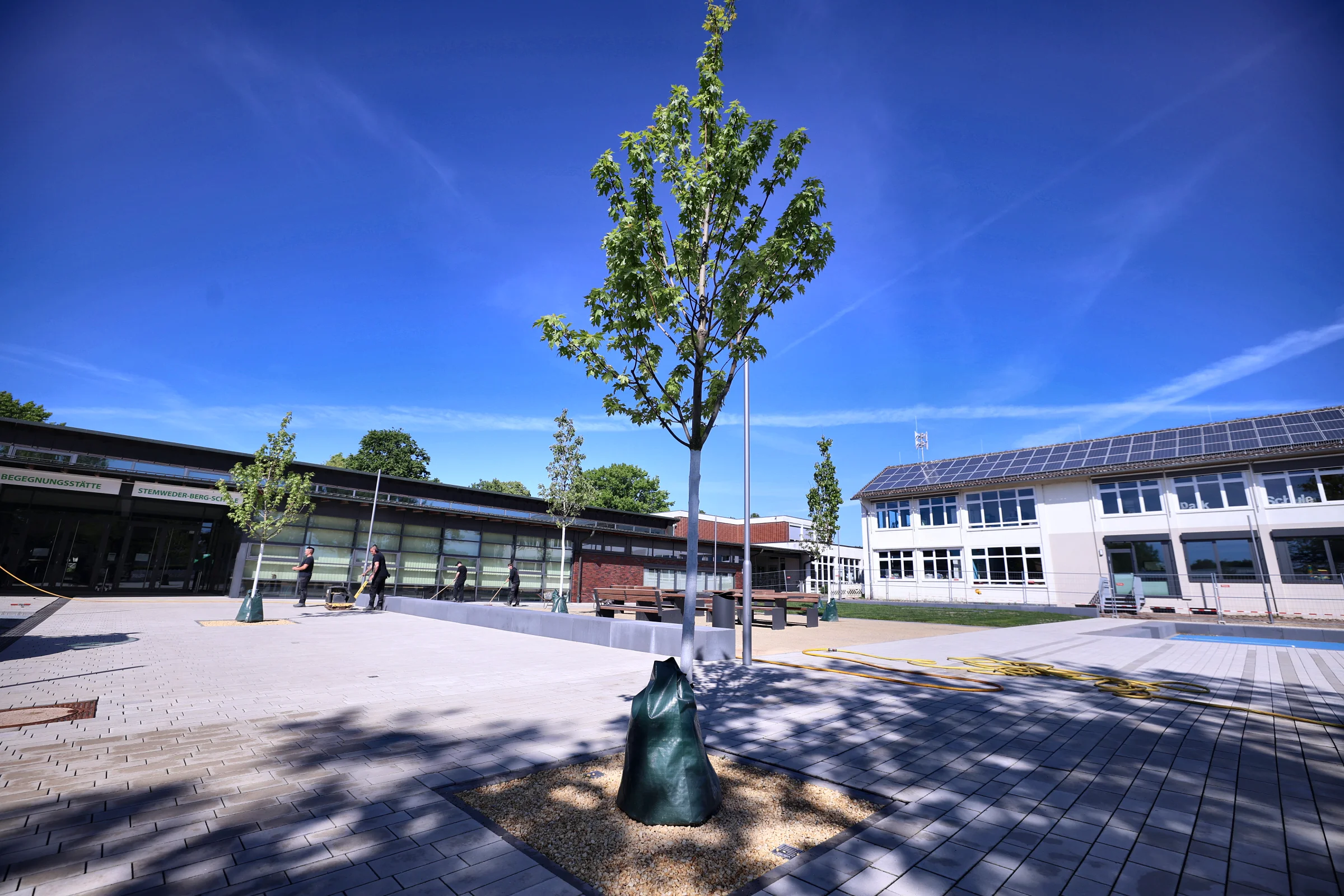 Gepflasterter Pausenhof mit Sitzgelegenheiten und Bepflanzung vor dem Schulgebäude