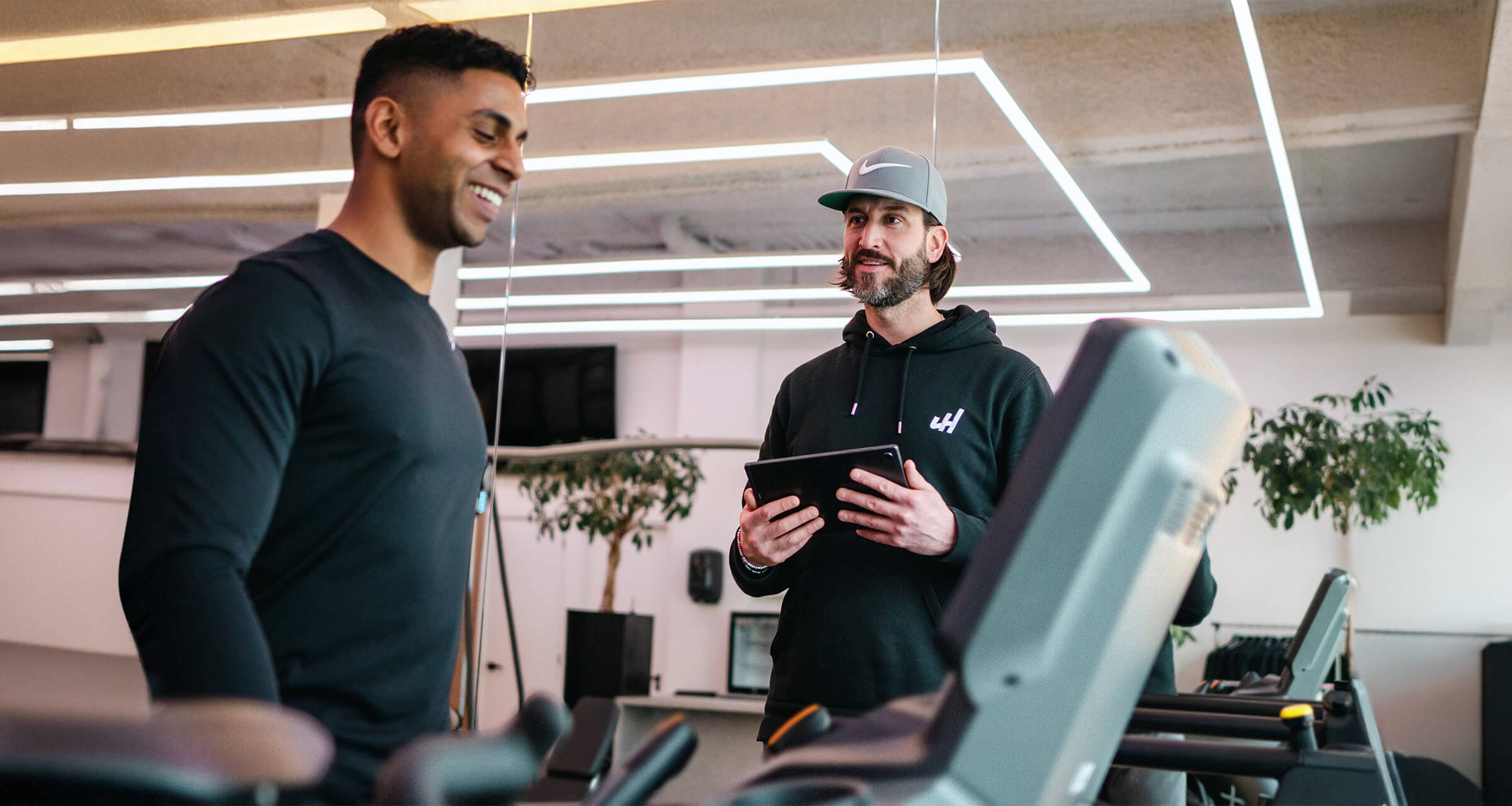 Een personal trainer in gesprek met een mannelijke cliënt op de loopband.