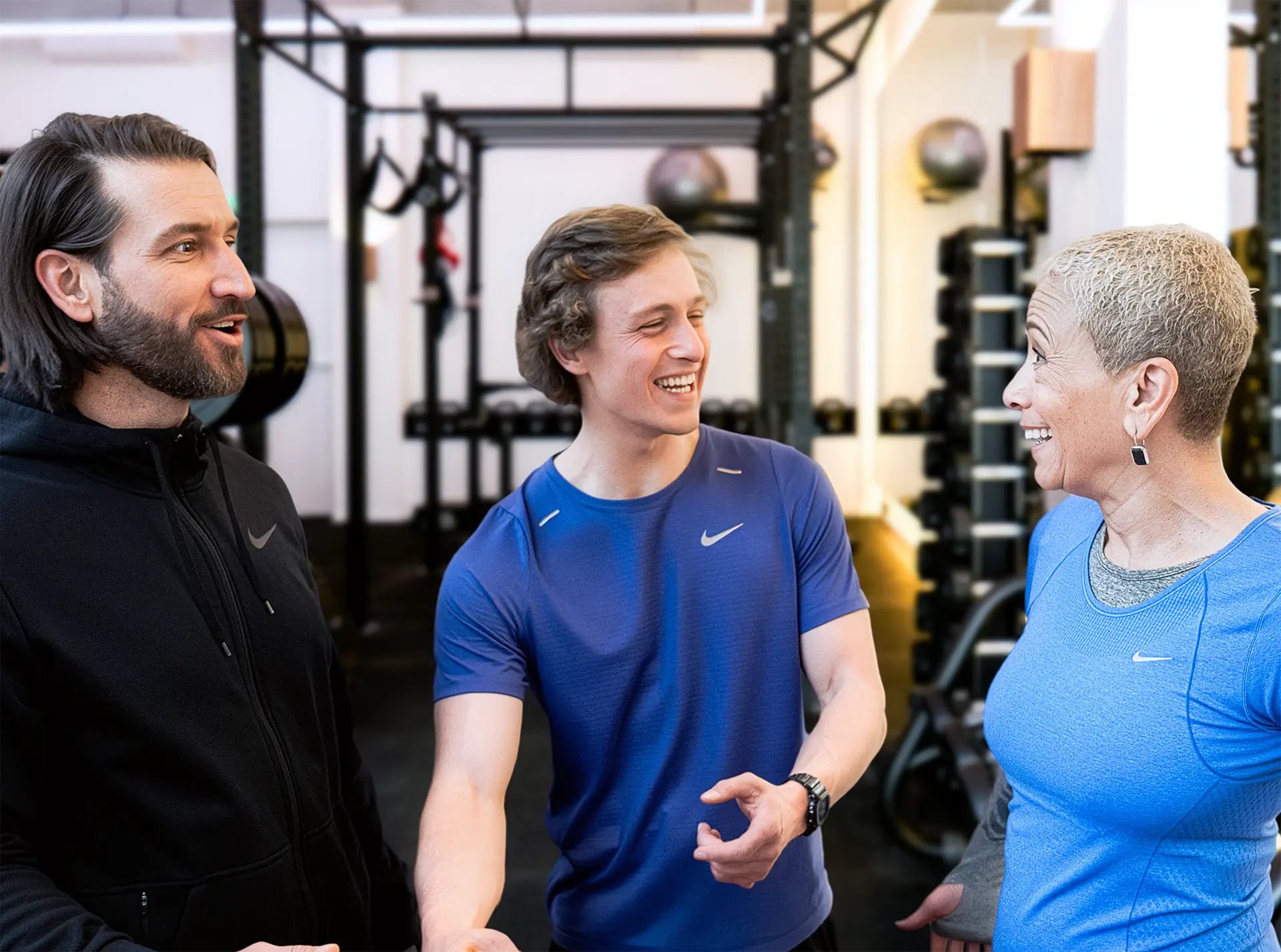 Drie mensen in sportkleding die in een sportschool lachend met elkaar praten.