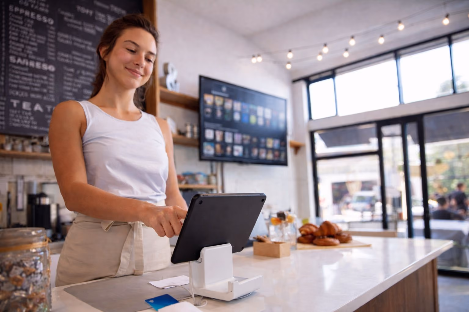 Empleado de una cafetería utilizando una tableta en un punto de venta, con música de fondo con licencia de Brandtrack sonando legalmente en un local comercial