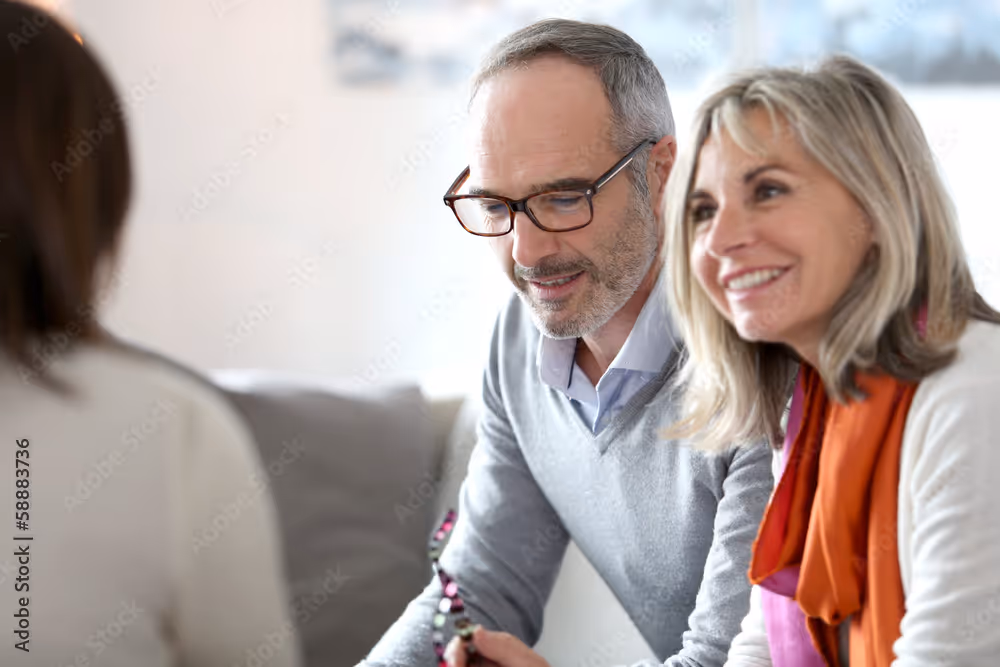Middle-aged couple sitting together, smiling, and engaging in conversation with a person facing them.