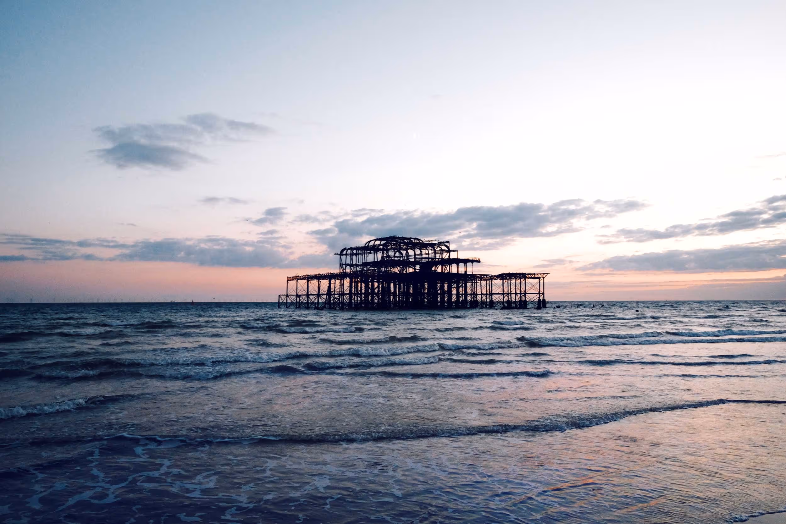 An old, rusted pier stands in the sea during sunset.