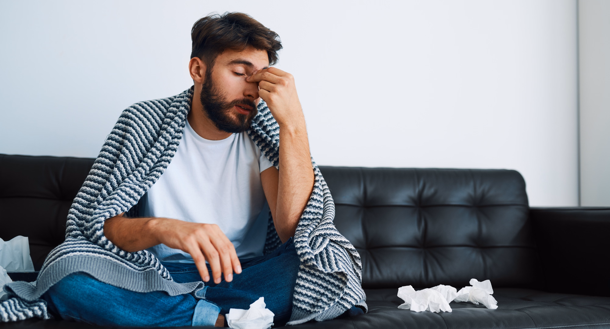 Čovjek sjedi na krevetu i drži nos, što ga boli jer ima sinusitis.