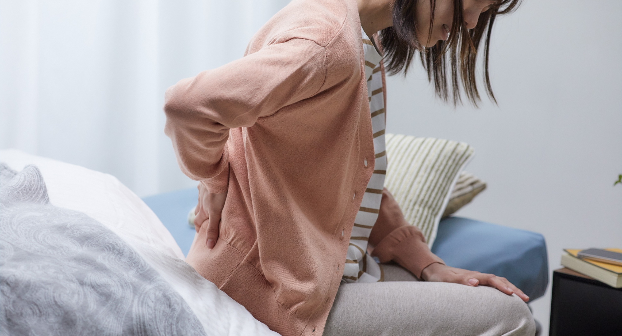 Žena sjedi i drži ruku na leđima koja je bole