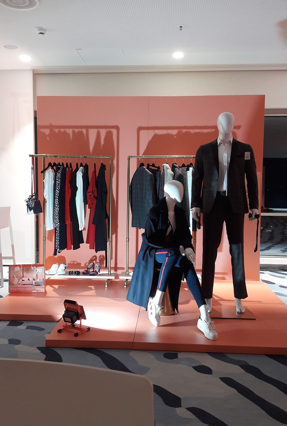Two mannequins wearing suits in front of a coat rack.