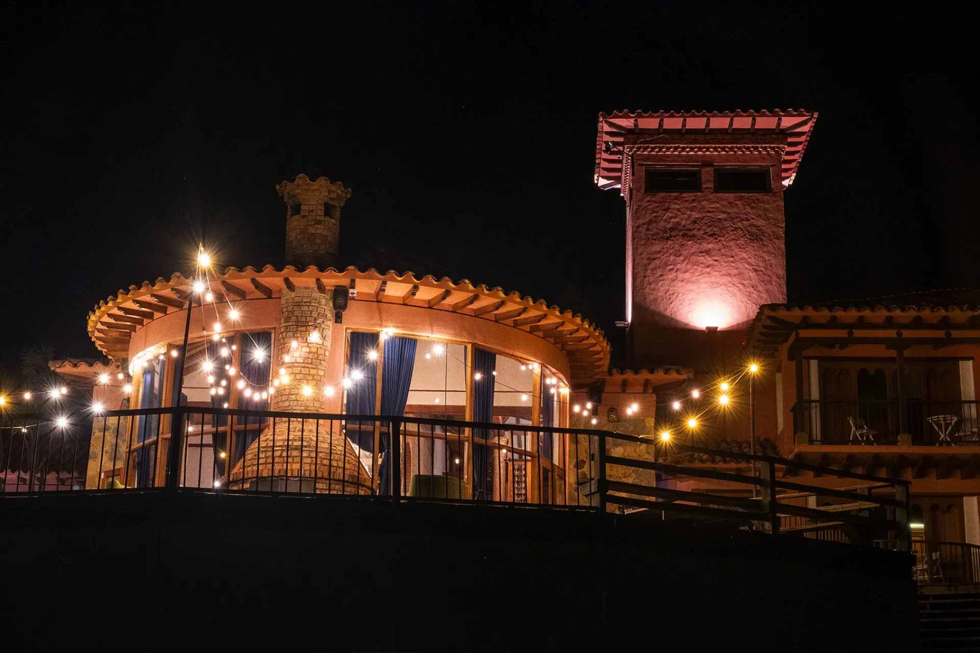 Terraza iluminada del Hotel 1572 El Origen en Villa de Leyva durante la noche, con arquitectura rústica, luces cálidas y espacios diseñados para descansar y desconectarse.”