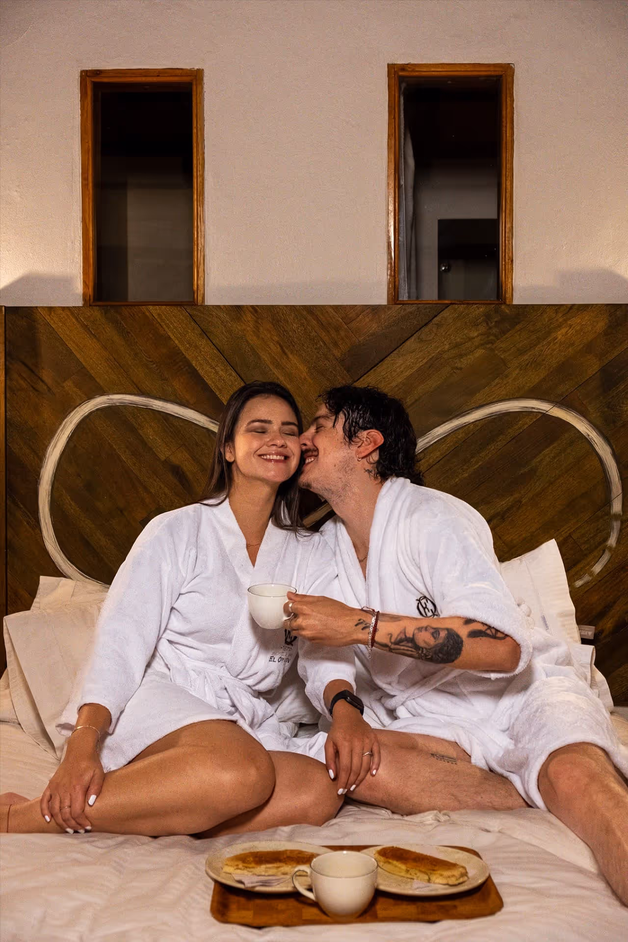 Pareja disfrutando una escapada romántica en una habitación del Hotel 1572 El Origen en Villa de Leyva, con desayuno en la cama y ambiente cálido de descanso y desconexión.
