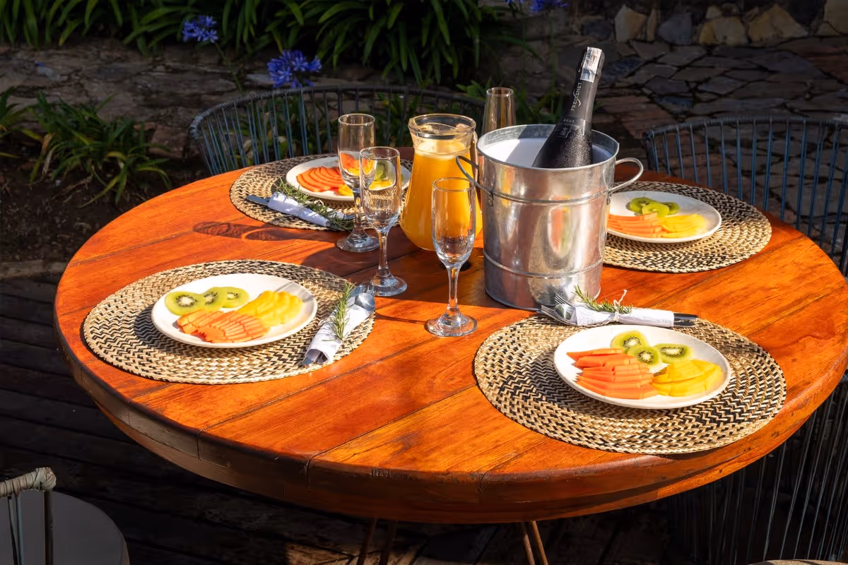 Mesa de desayuno al aire libre en Hotel 1572 El Origen con frutas frescas, bebidas y ambiente natural, ideal para compartir una experiencia de descanso en Villa de Leyva.”
