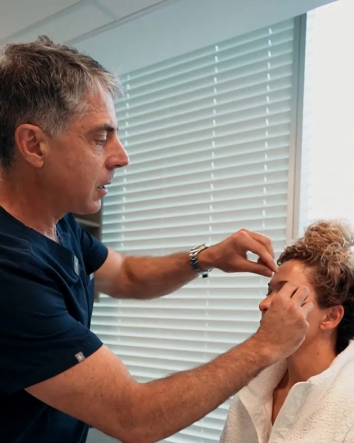 Dr. Buonassisi examining a patient's upper eyelid in a consultation room