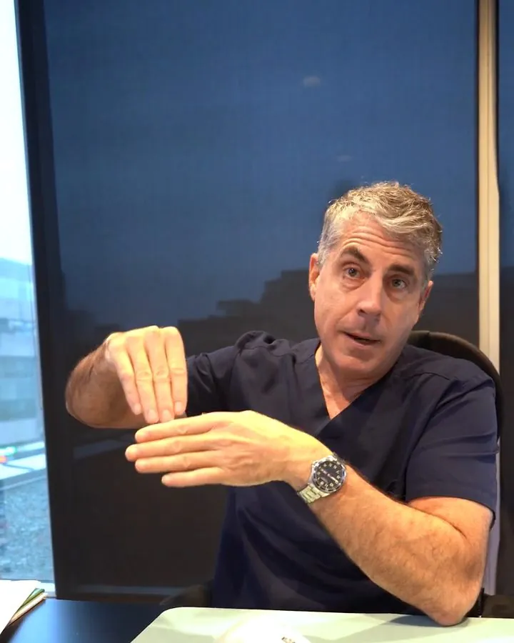 Dr. Buonassisi at his desk, showing with his hands how eyelid skin folds