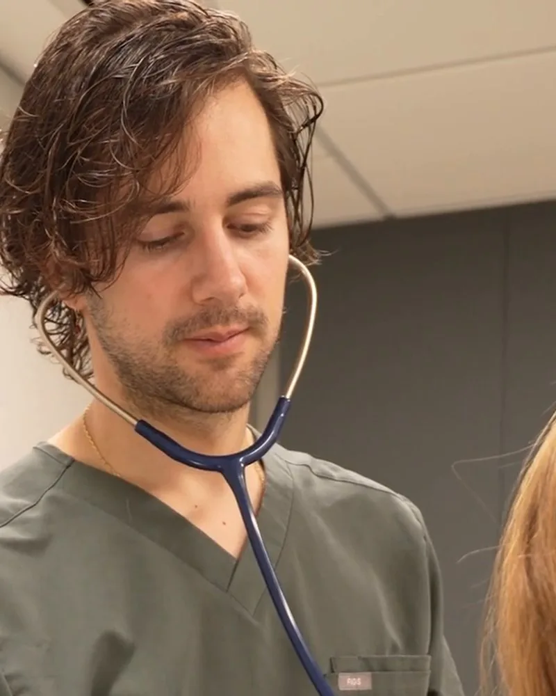 Dr. Masschelein in surgical scrubs with a stethoscope, seeing a patient