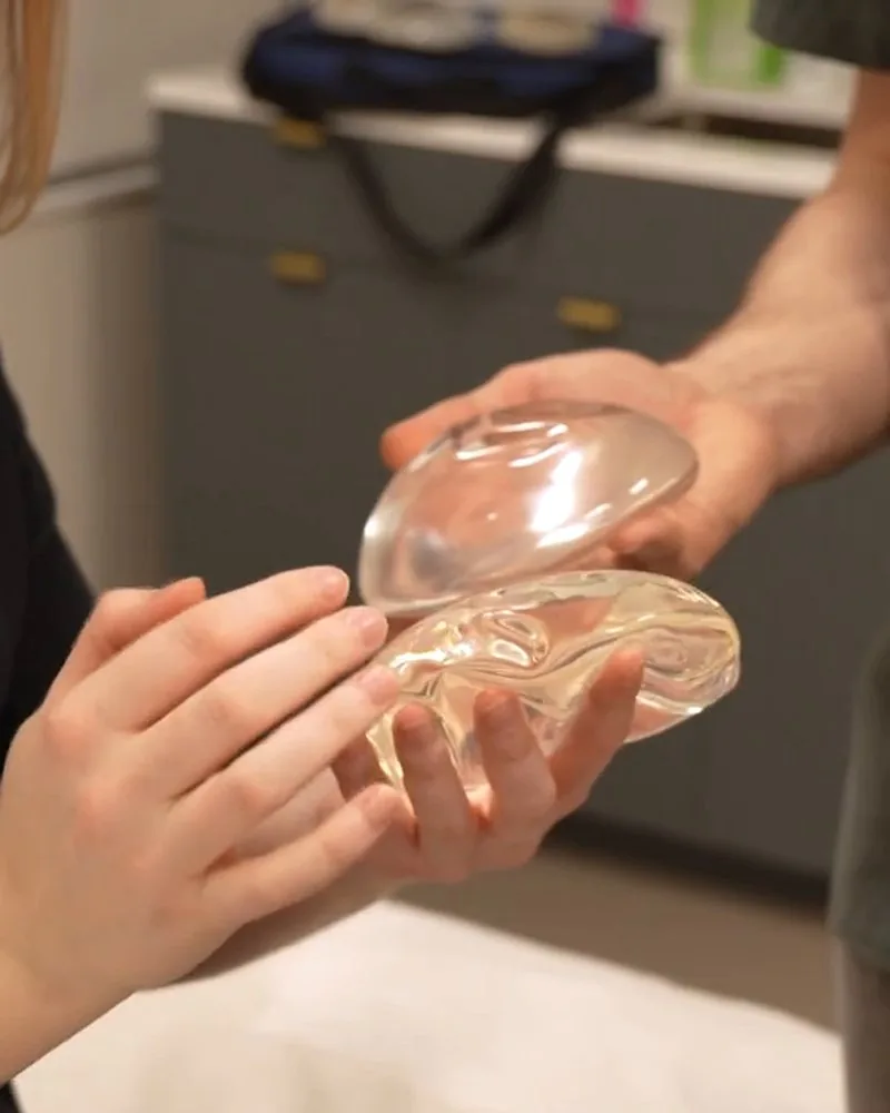 Two hands holding clear breast implant sizers in a consultation room