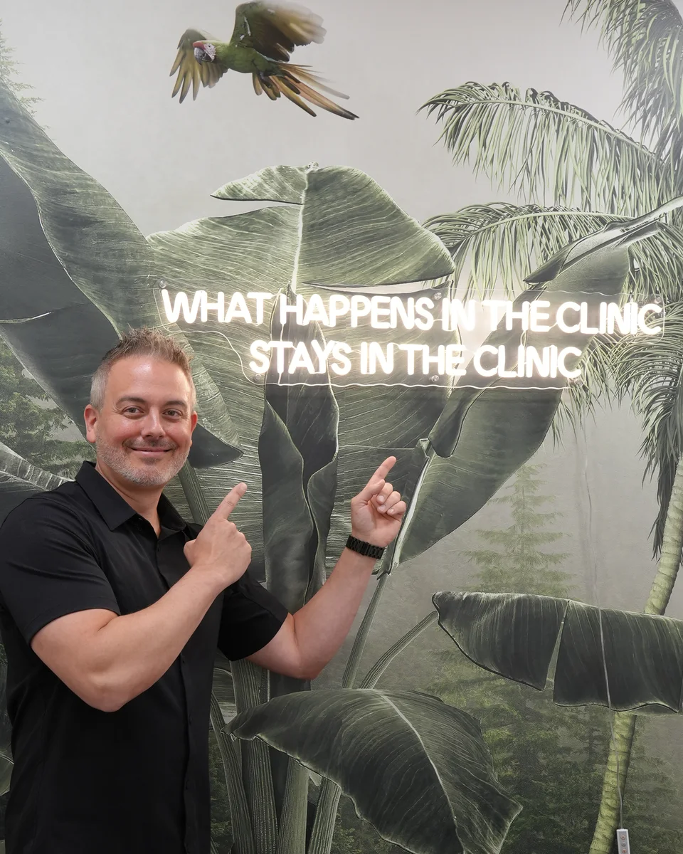 A patient smiling beside the neon sign What happens in the clinic stays in the clinic at 8 West Clinic