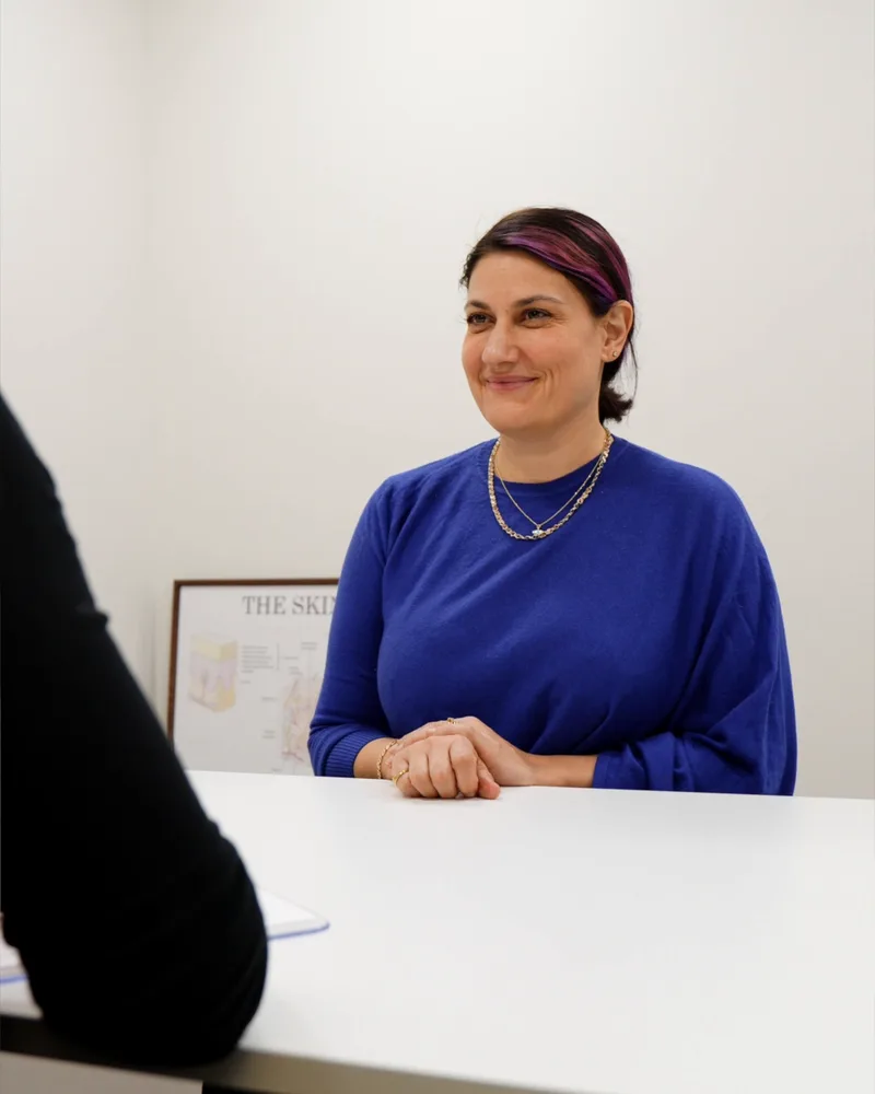 A client in a blue top smiling across the consultation table at 8 West Clinic